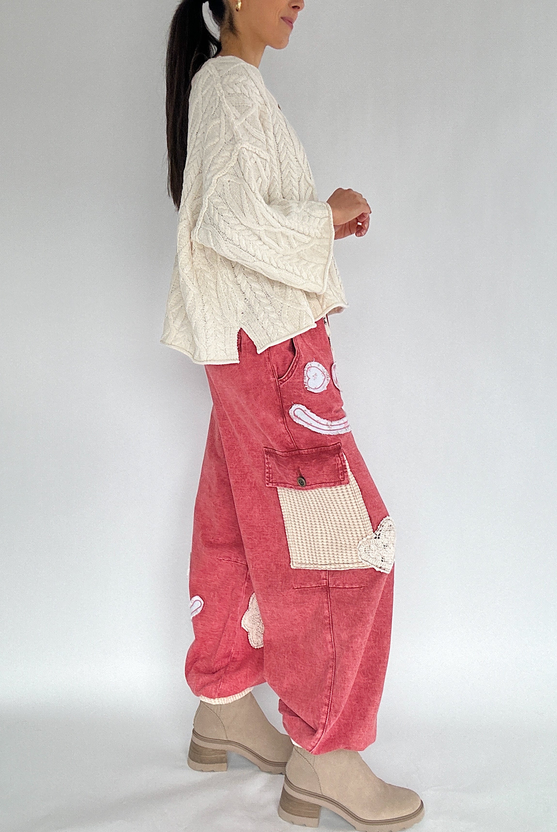 Person wearing a cream sweater and red pants with a white background side view