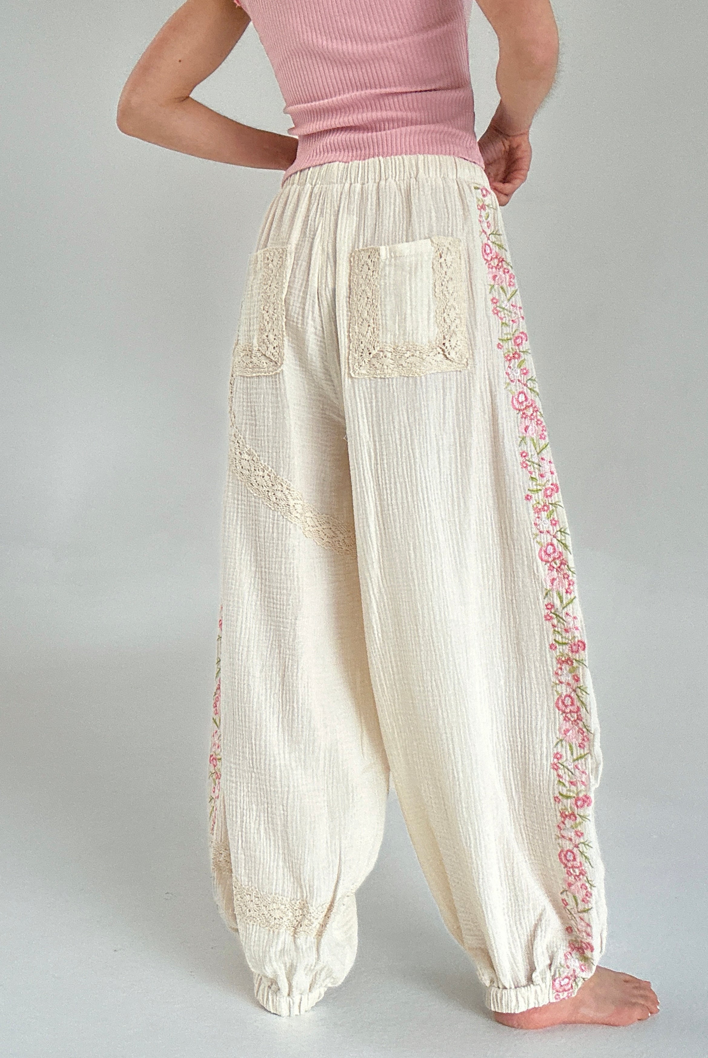 Person wearing cream-colored pants with floral embroidery on a plain background showing back pocket details