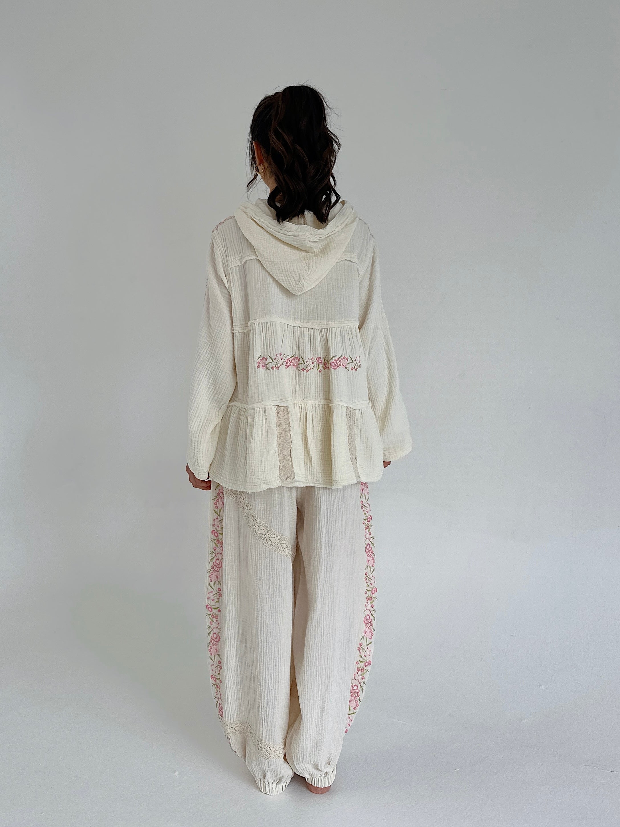 Person wearing a cream-colored outfit with floral embroidery on a plain background showing back