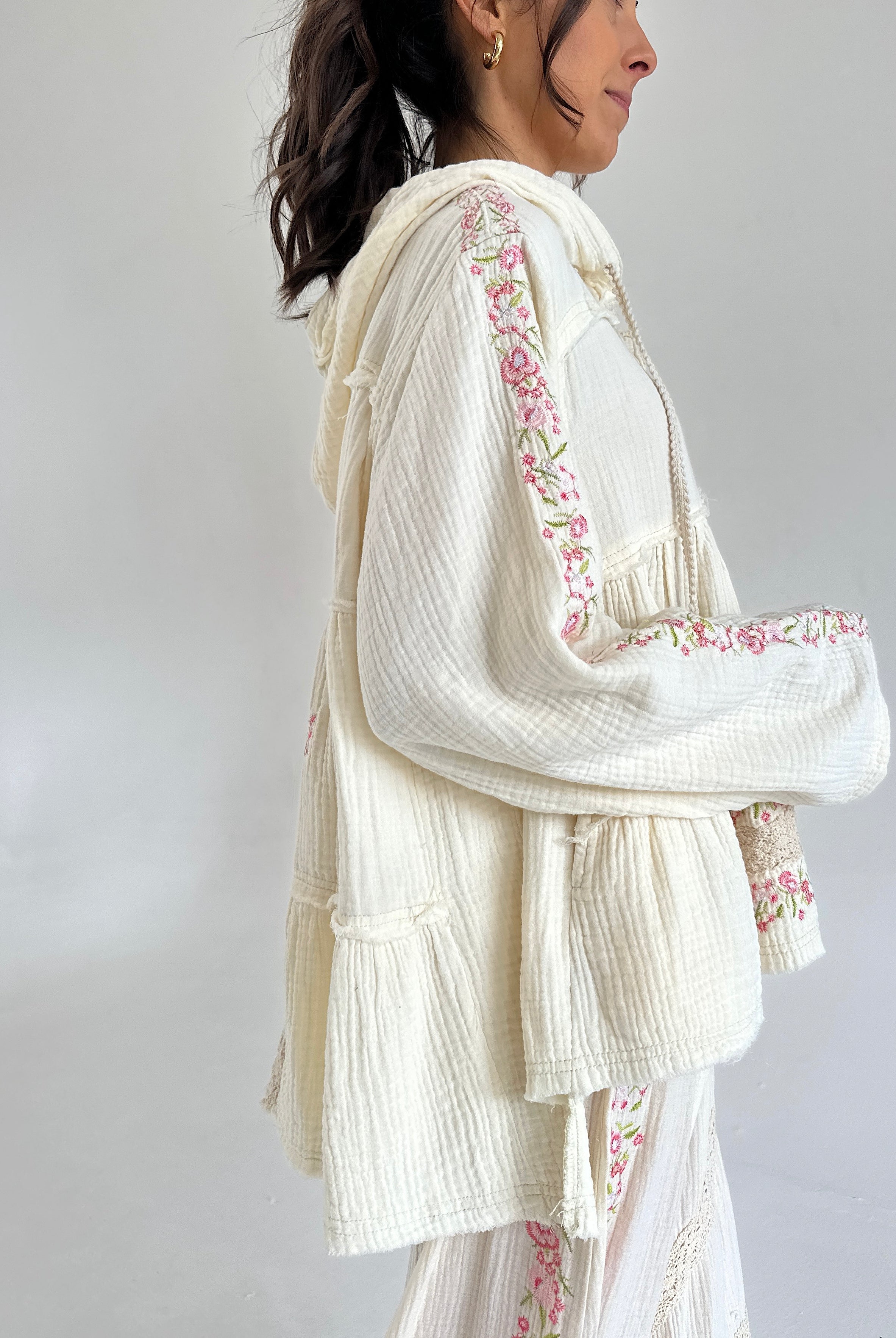 Woman wearing a white embroidered outfit with a plain background showing side view