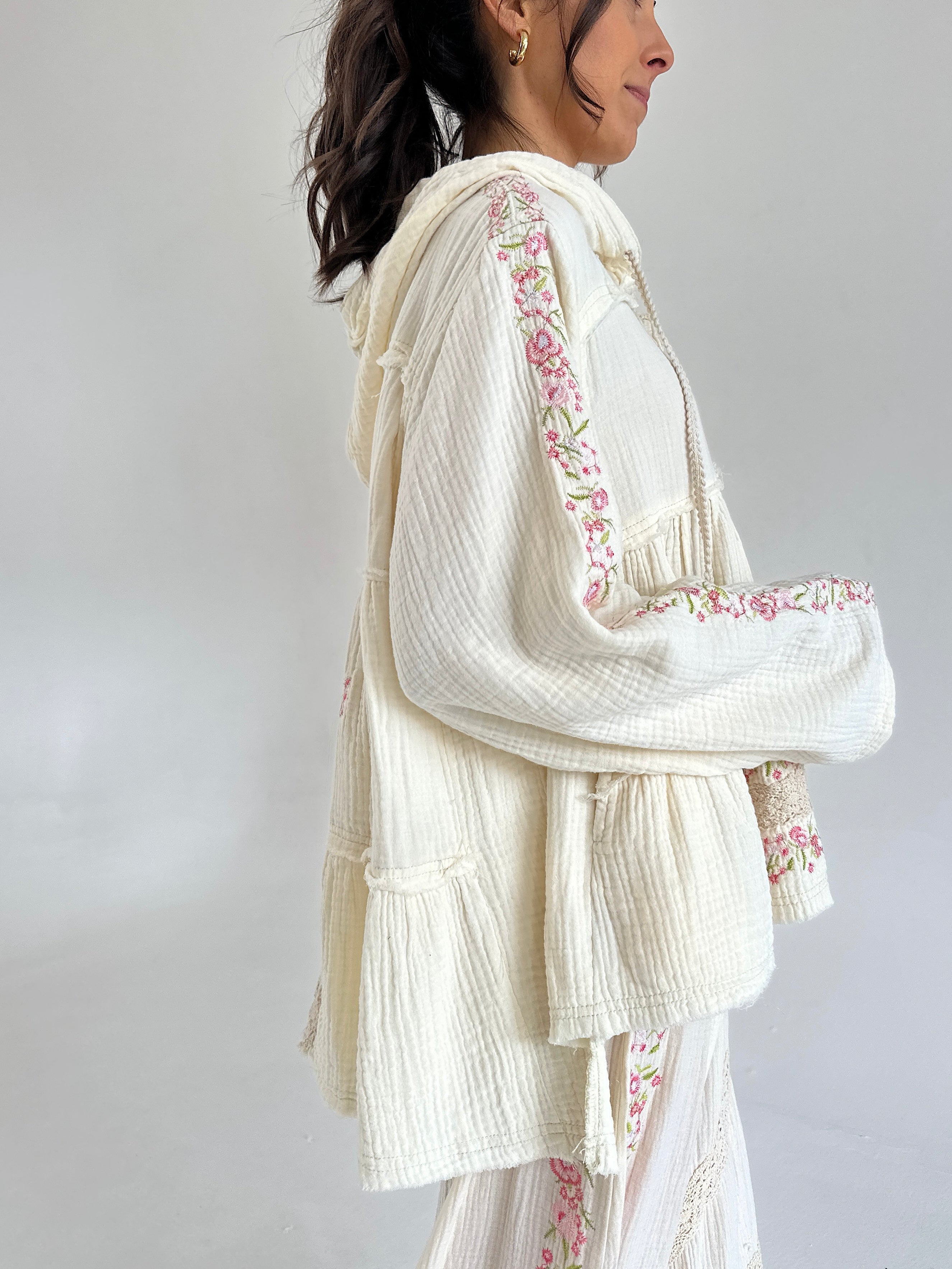 Woman wearing a white embroidered outfit with a plain background showing side view