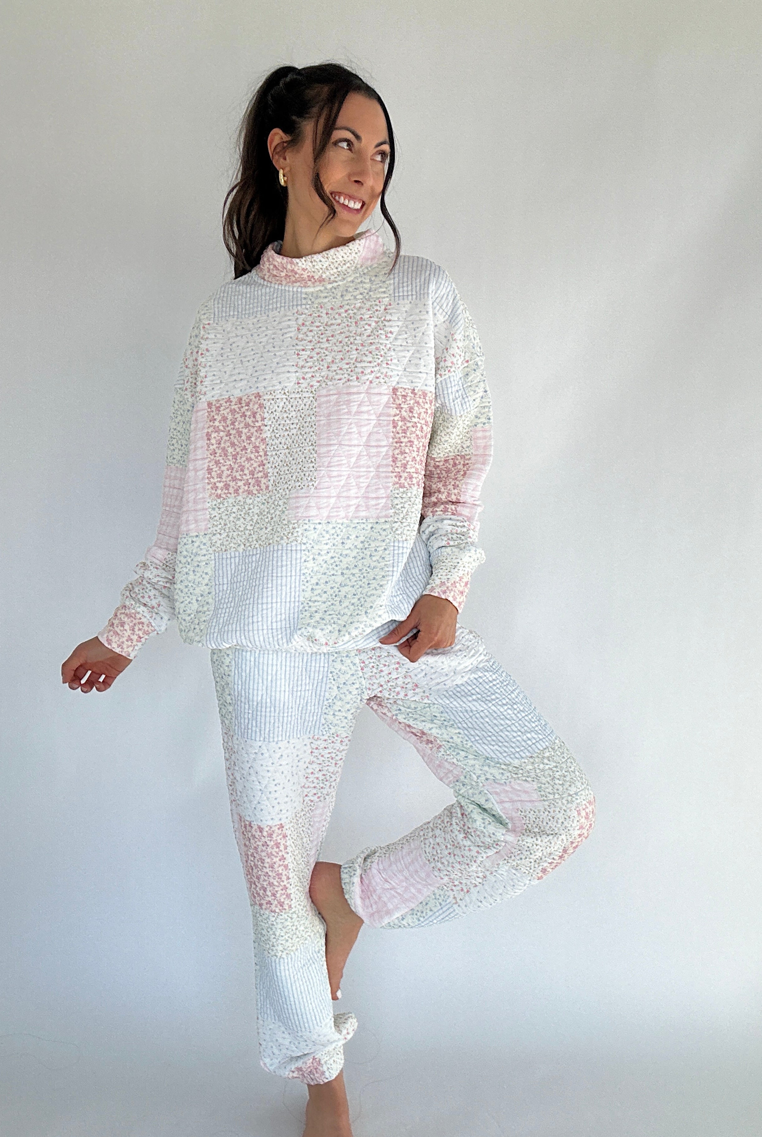 Woman wearing a white and pink quilted patterned mock neck and jogger set against a plain background