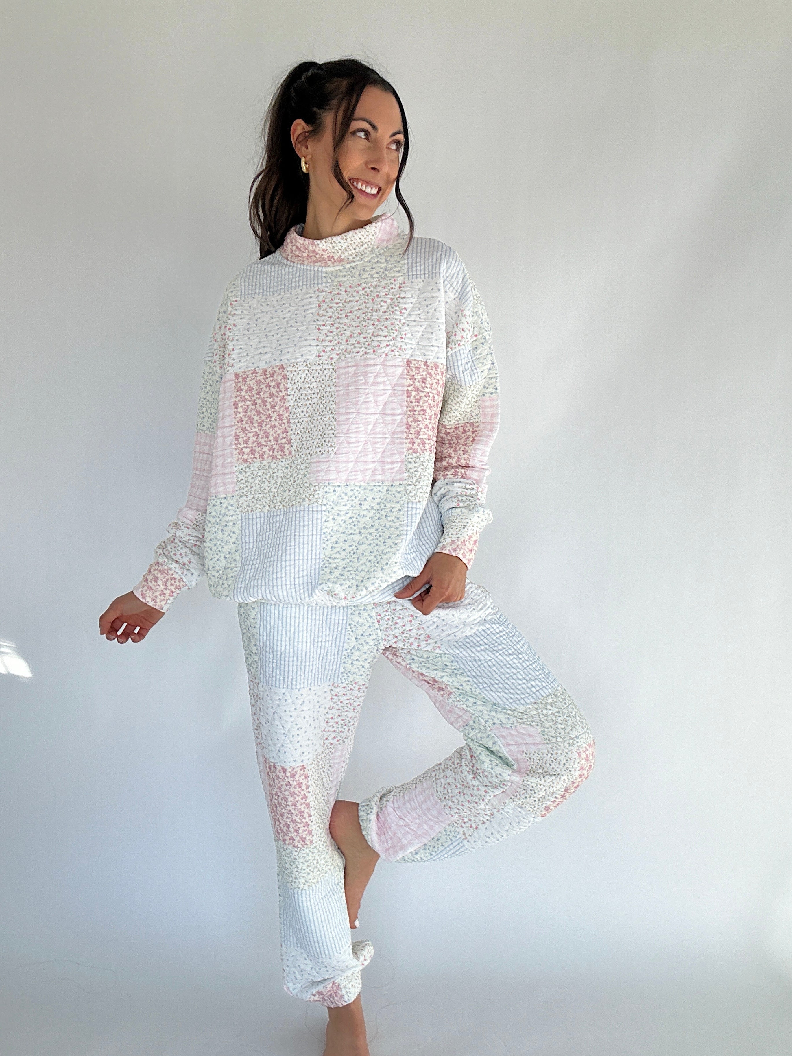 Woman wearing a white and pink quilted patterned mock neck and jogger set against a plain background