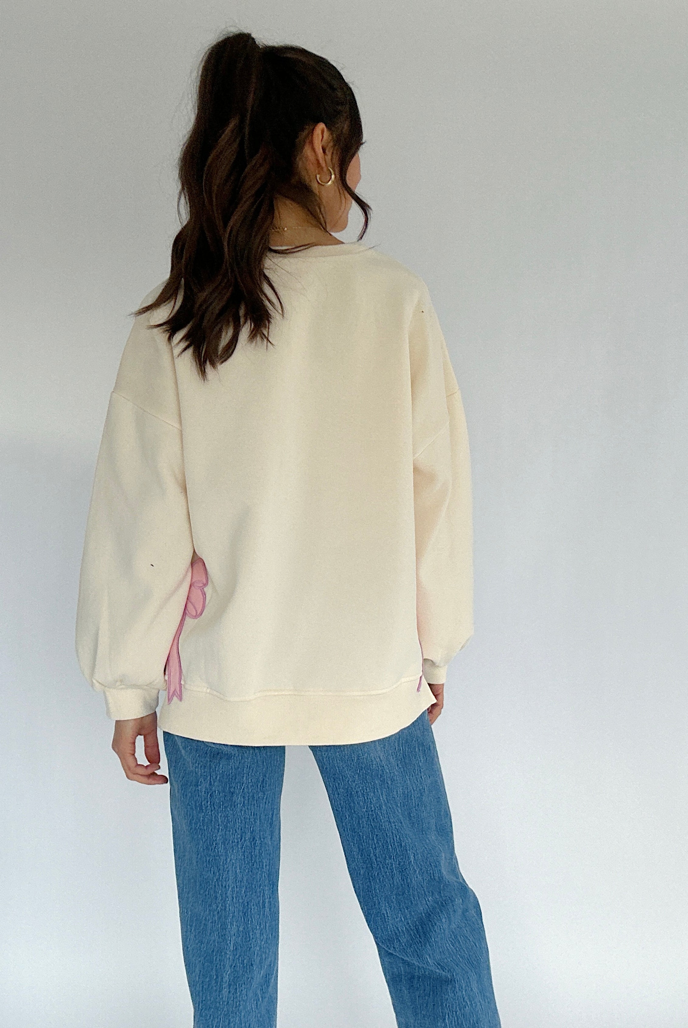 Person wearing a cream sweater and blue jeans against a white background
