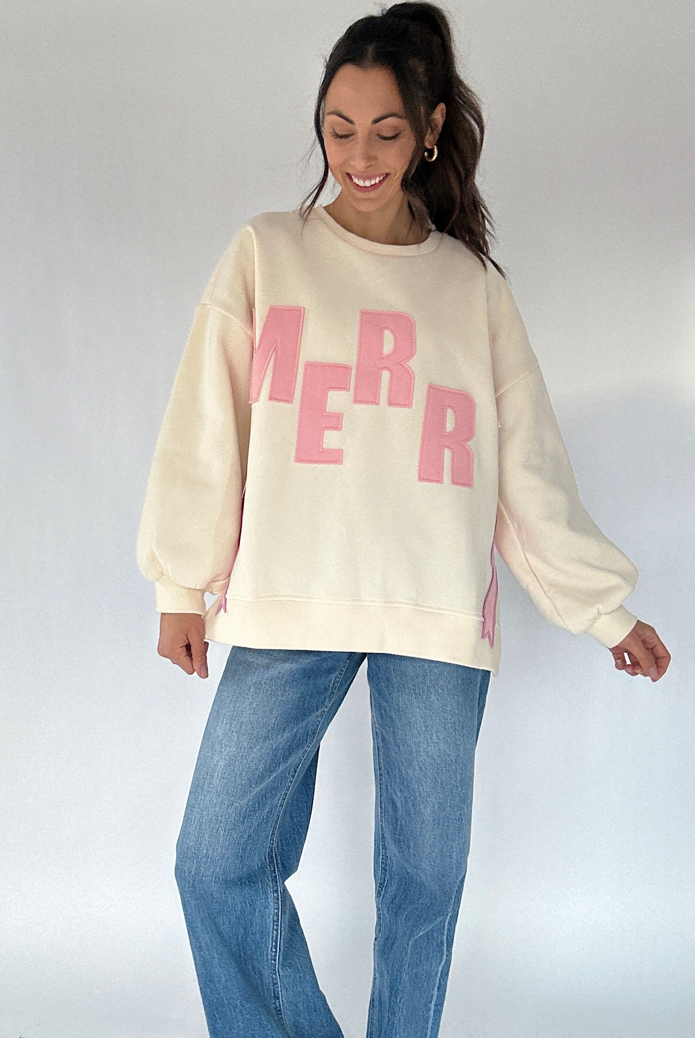Woman wearing a cream sweatshirt with pink text and blue jeans on a white background