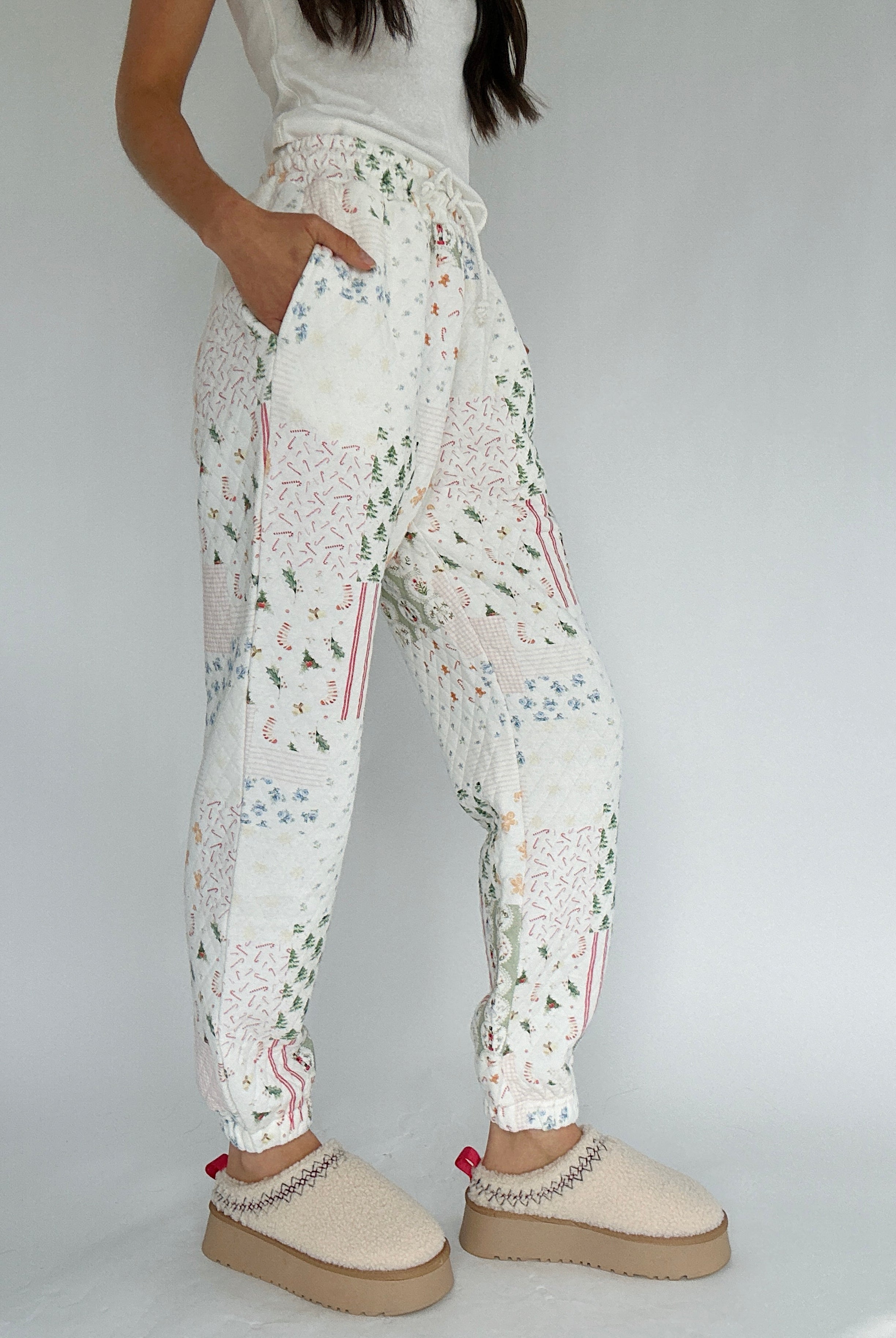 Person wearing white quilted holiday-patterned jogger pants with beige clogs on a plain background