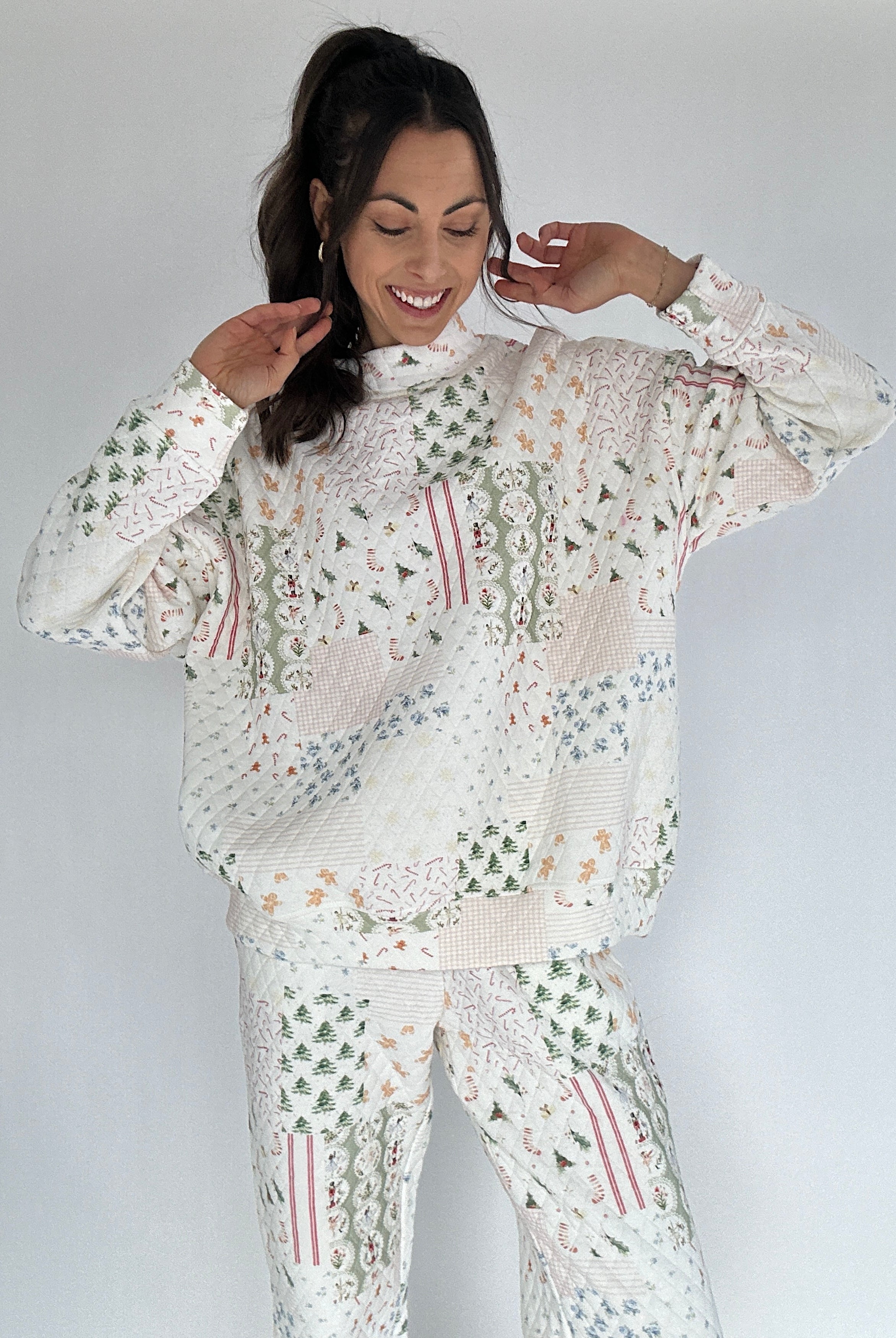 Woman wearing a white quilted mock neck with mixed holiday patterns and matching pants against a plain background