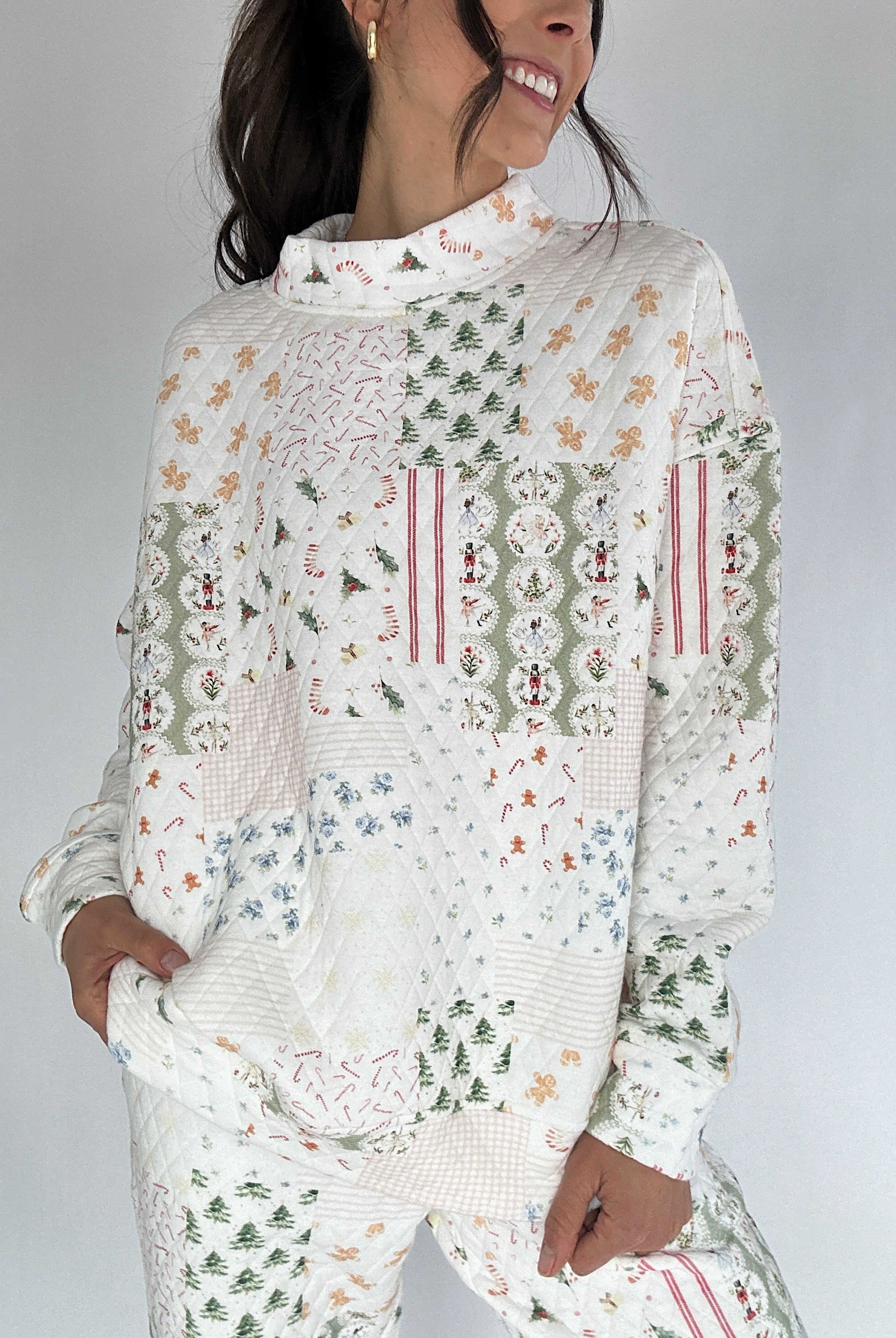 Woman wearing a white holiday patterned quilted mock neck pullover against a gray background
