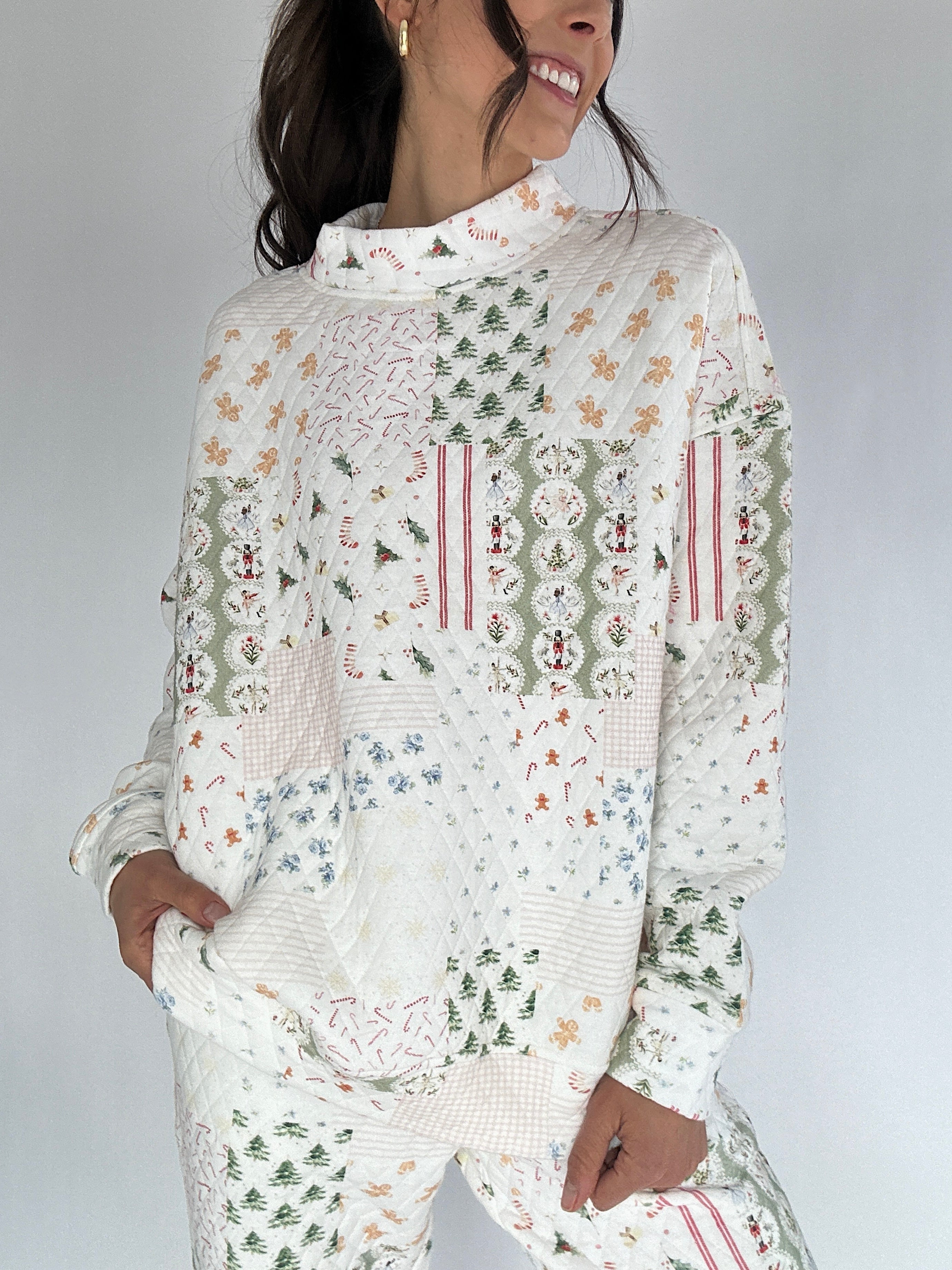 Woman wearing a white holiday patterned quilted mock neck pullover against a gray background