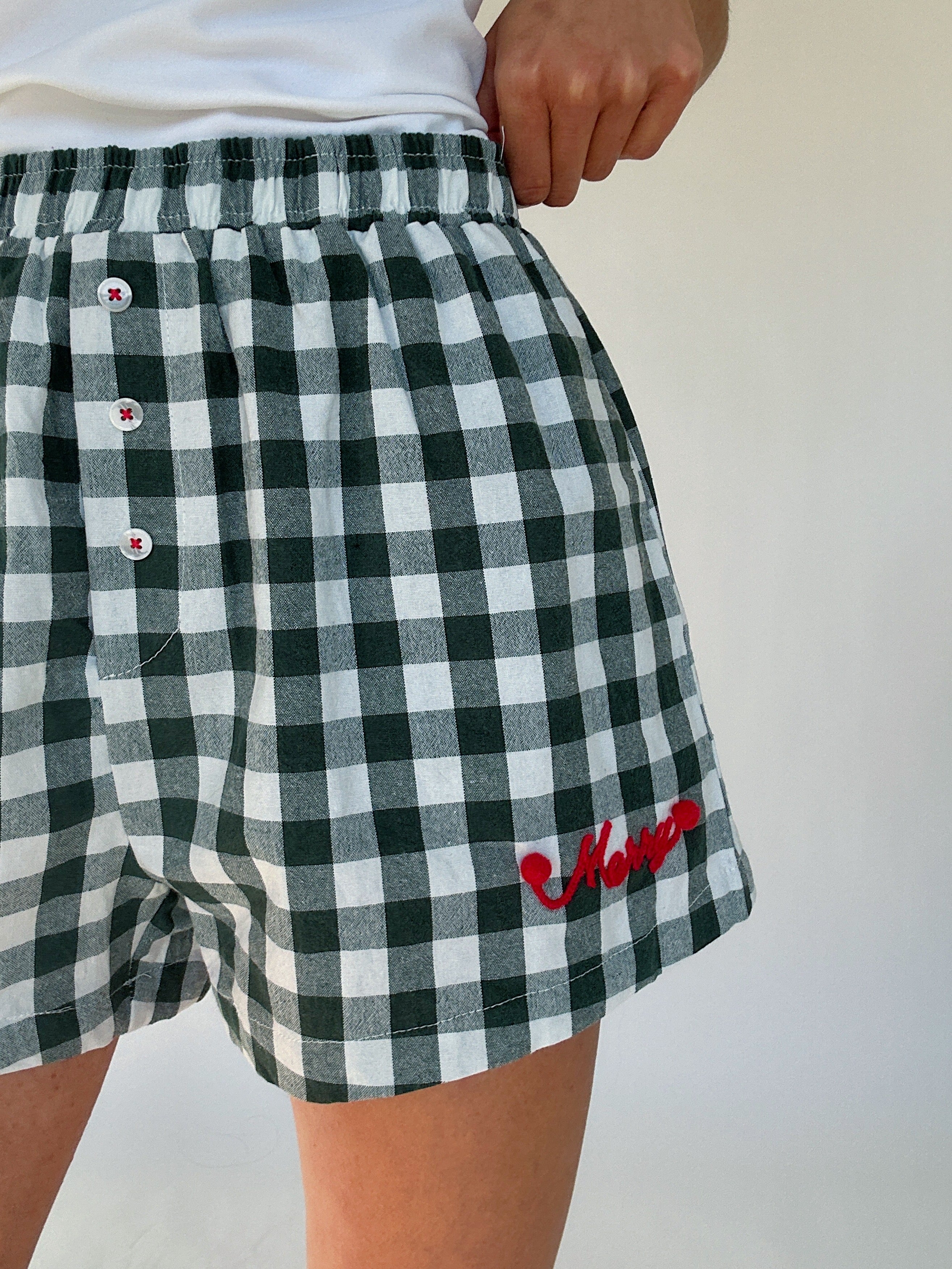 Green and white checkered boxer shorts with buttons and red "merry" lettering on a plain background
