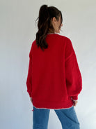 Person wearing a red sweater and blue jeans against a white background showing back view