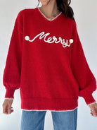 Red sweater with white 'Merry' text in cursive worn by a woman in jeans on a white background
