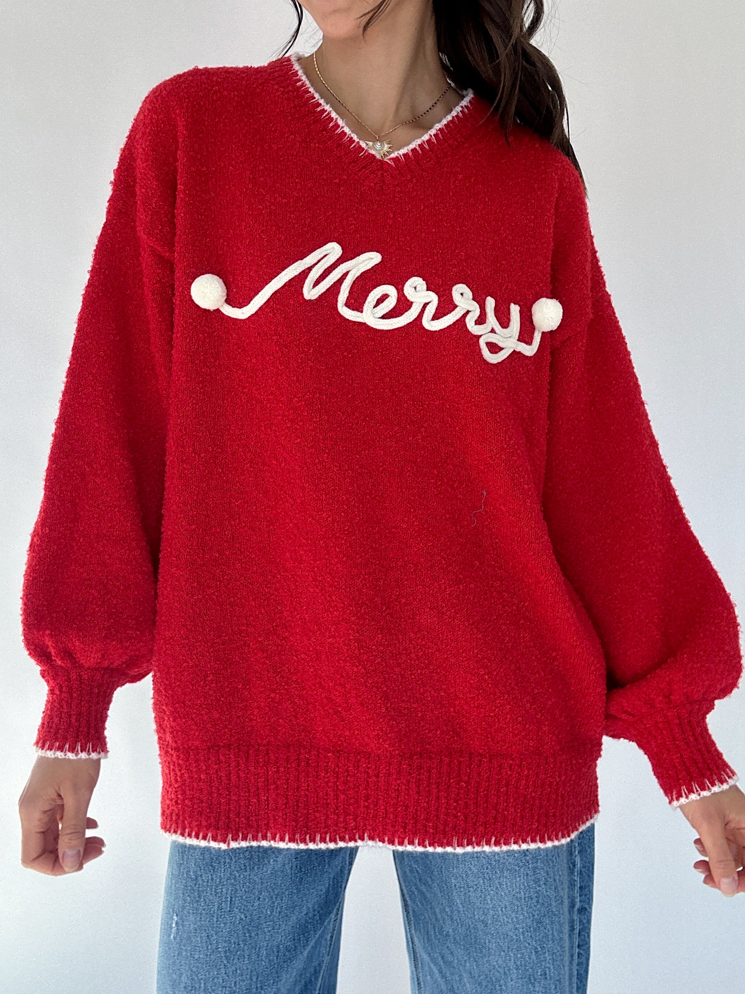 Red sweater with white 'Merry' text in cursive worn by a woman in jeans on a white background