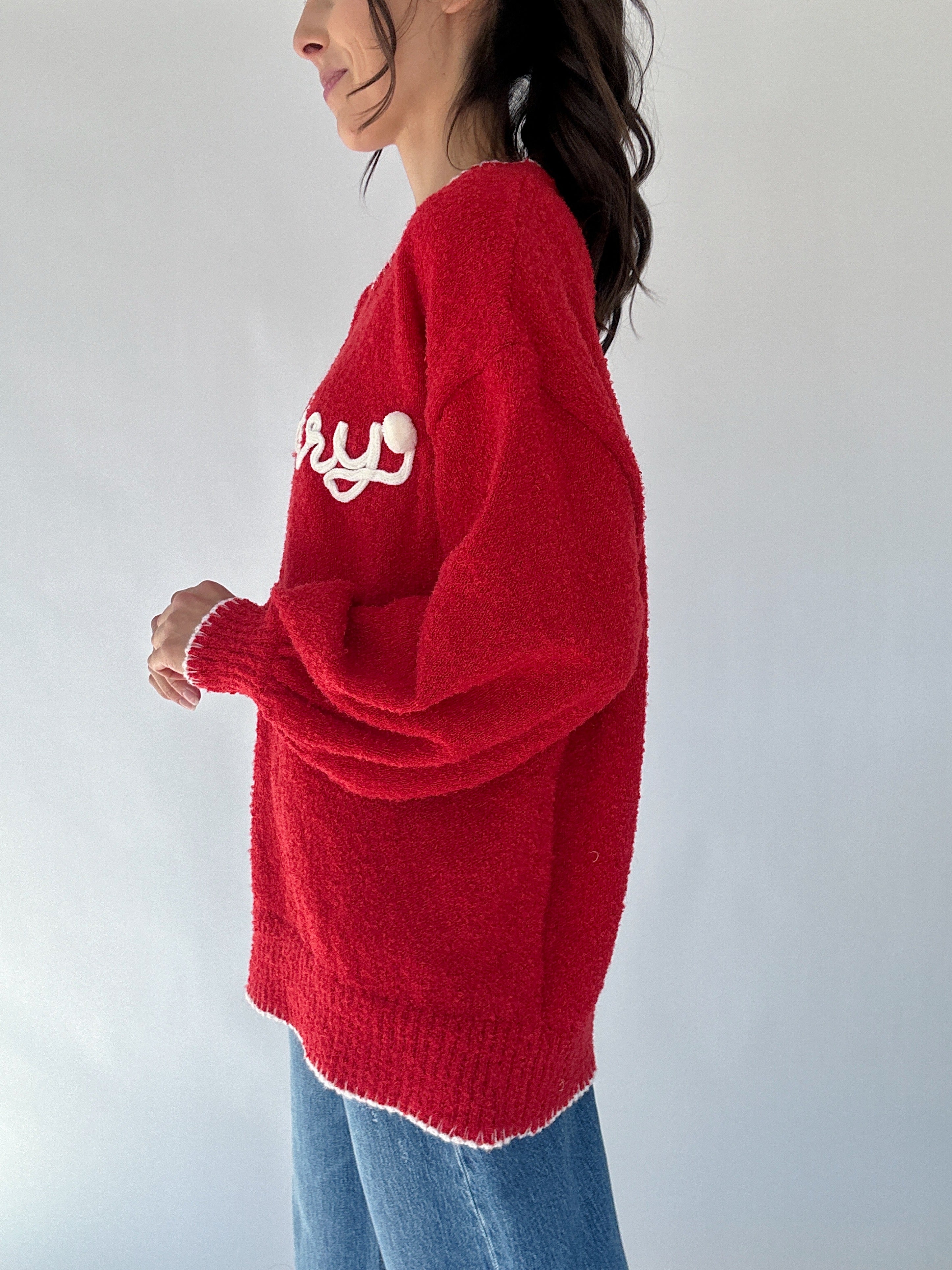 Person wearing a red sweater with white "merry" text and pompom detail on a plain background to show side view