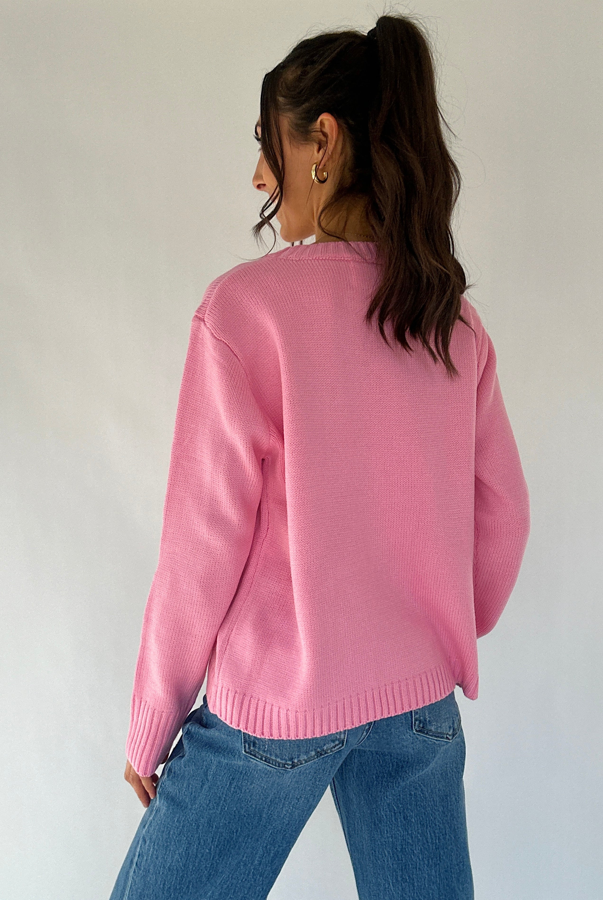 Person wearing a pink sweater and blue jeans against a white background from back