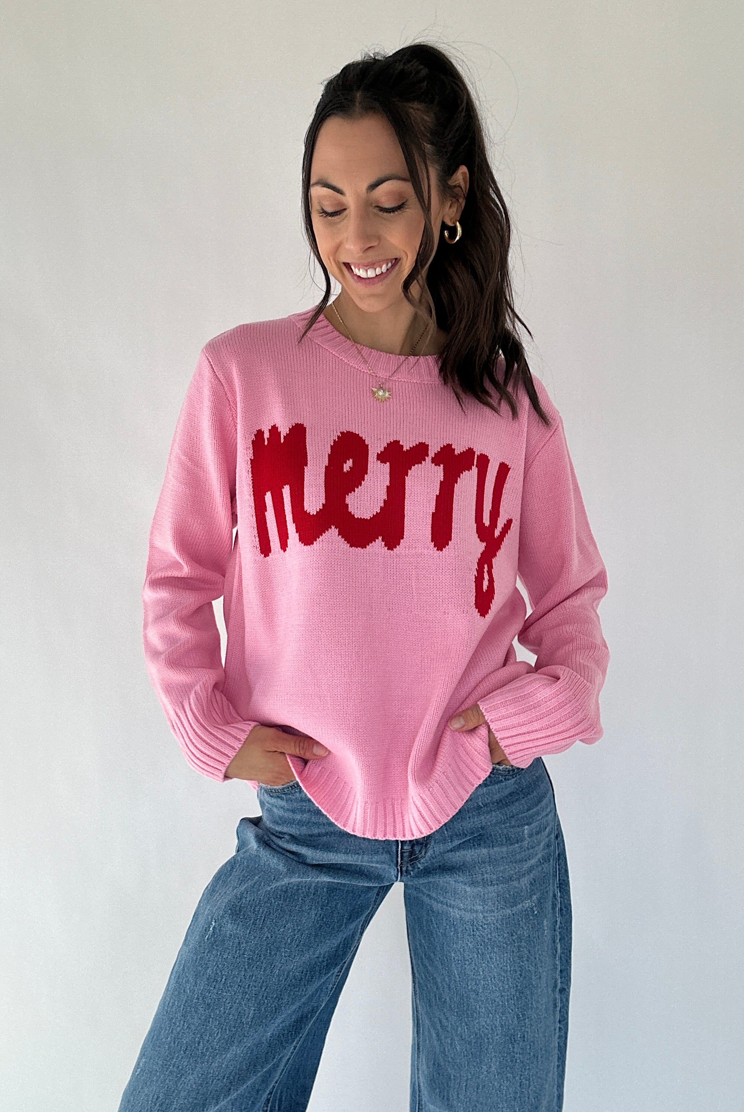 Woman wearing a pink sweater with 'merry' text against a plain background