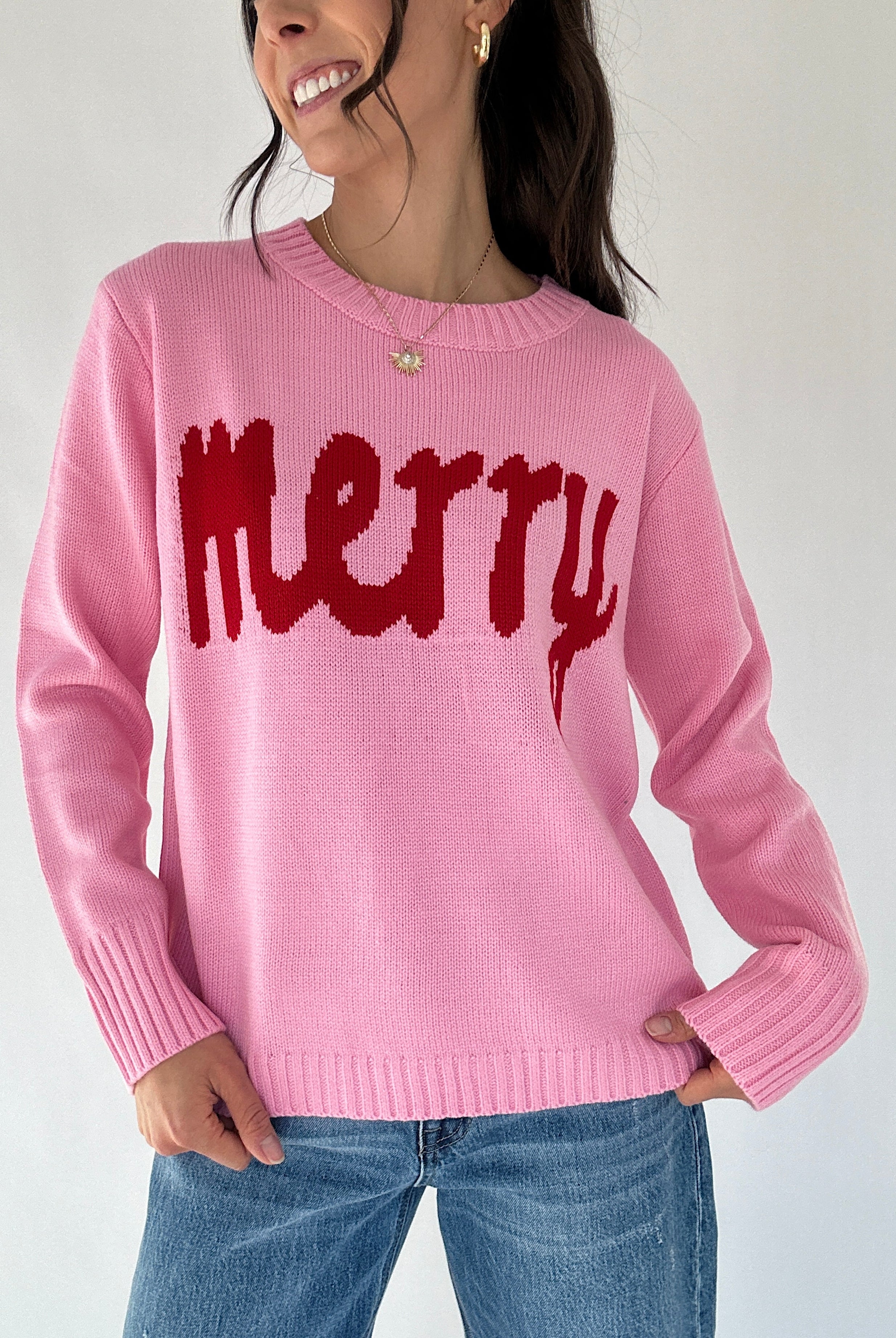 Person wearing a pink sweater with red 'merry' text on a plain background