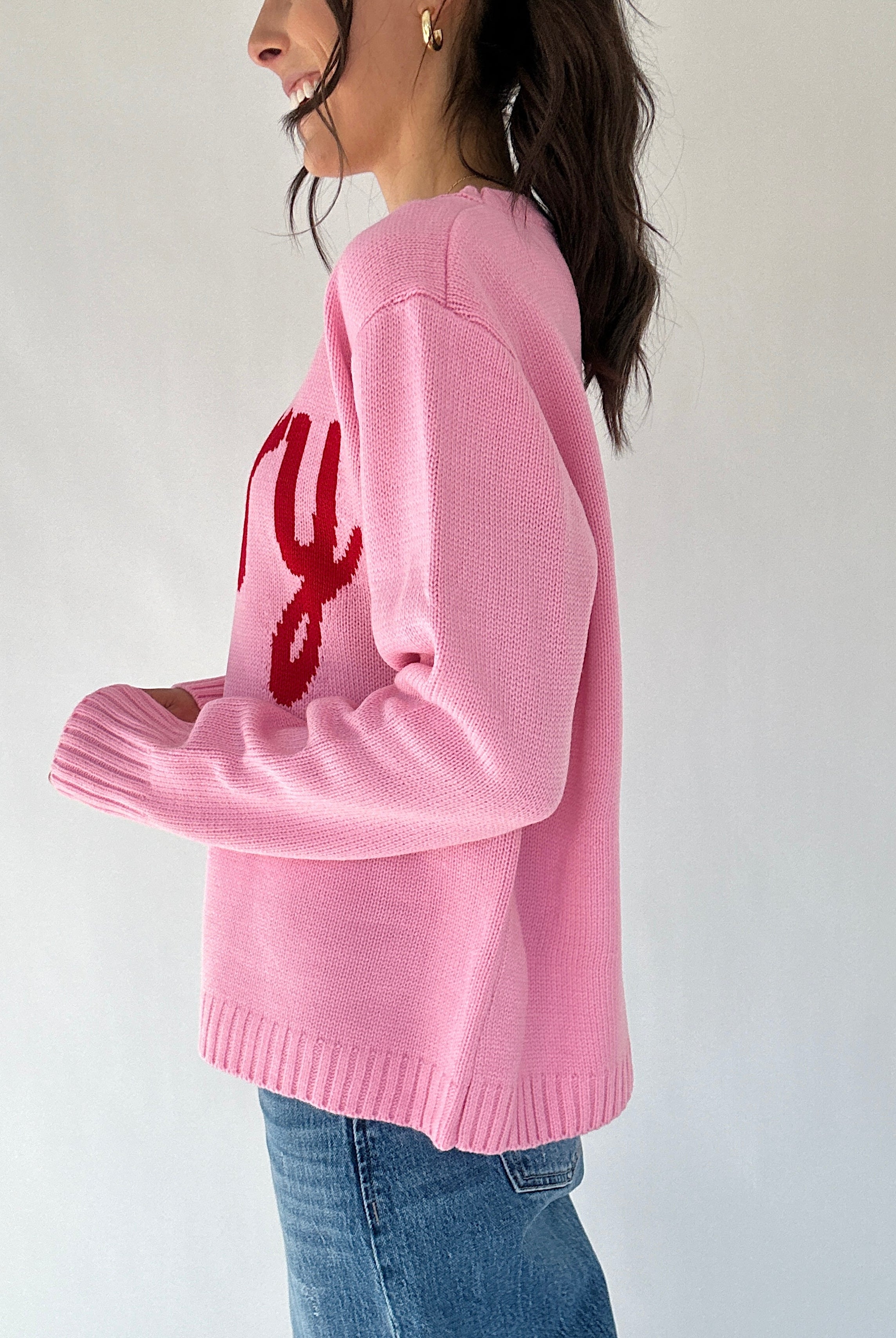 Person wearing a pink sweater with red text design on a white background from side