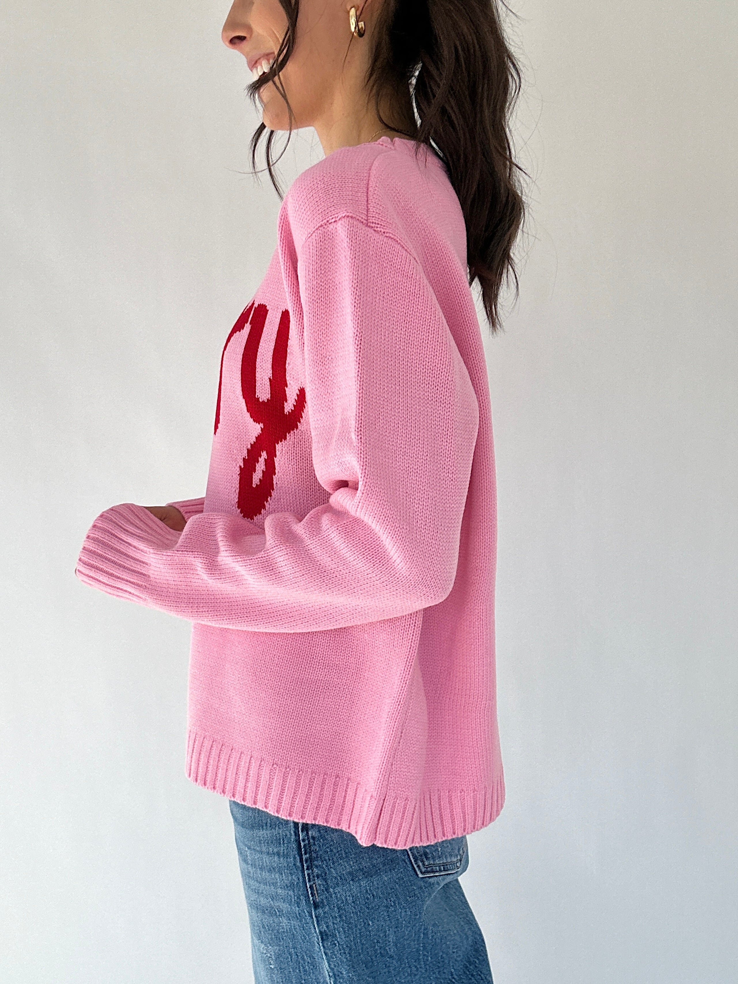 Person wearing a pink sweater with red text design on a white background from side