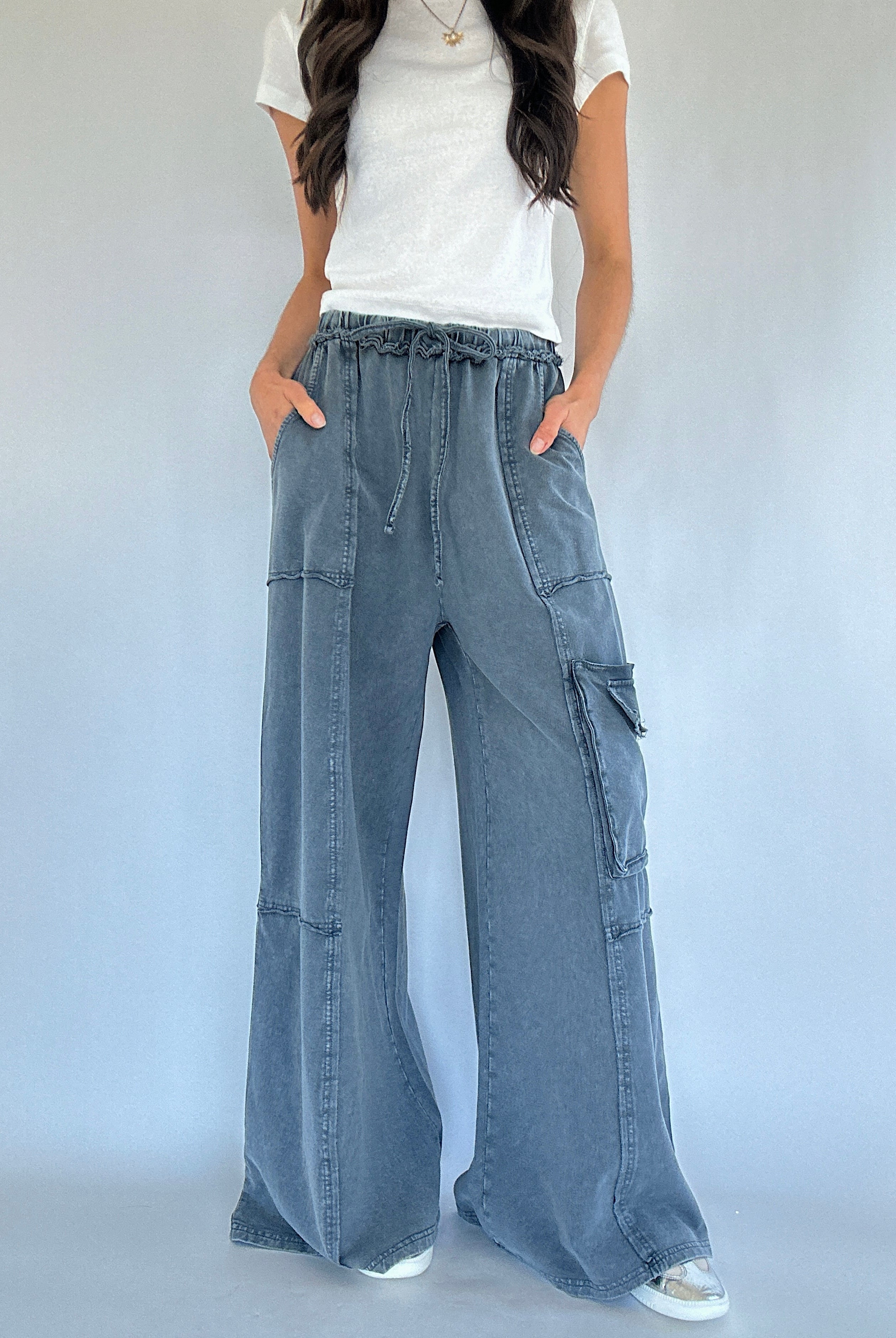 Person wearing smoke blue cargo pants and a white top on a plain background