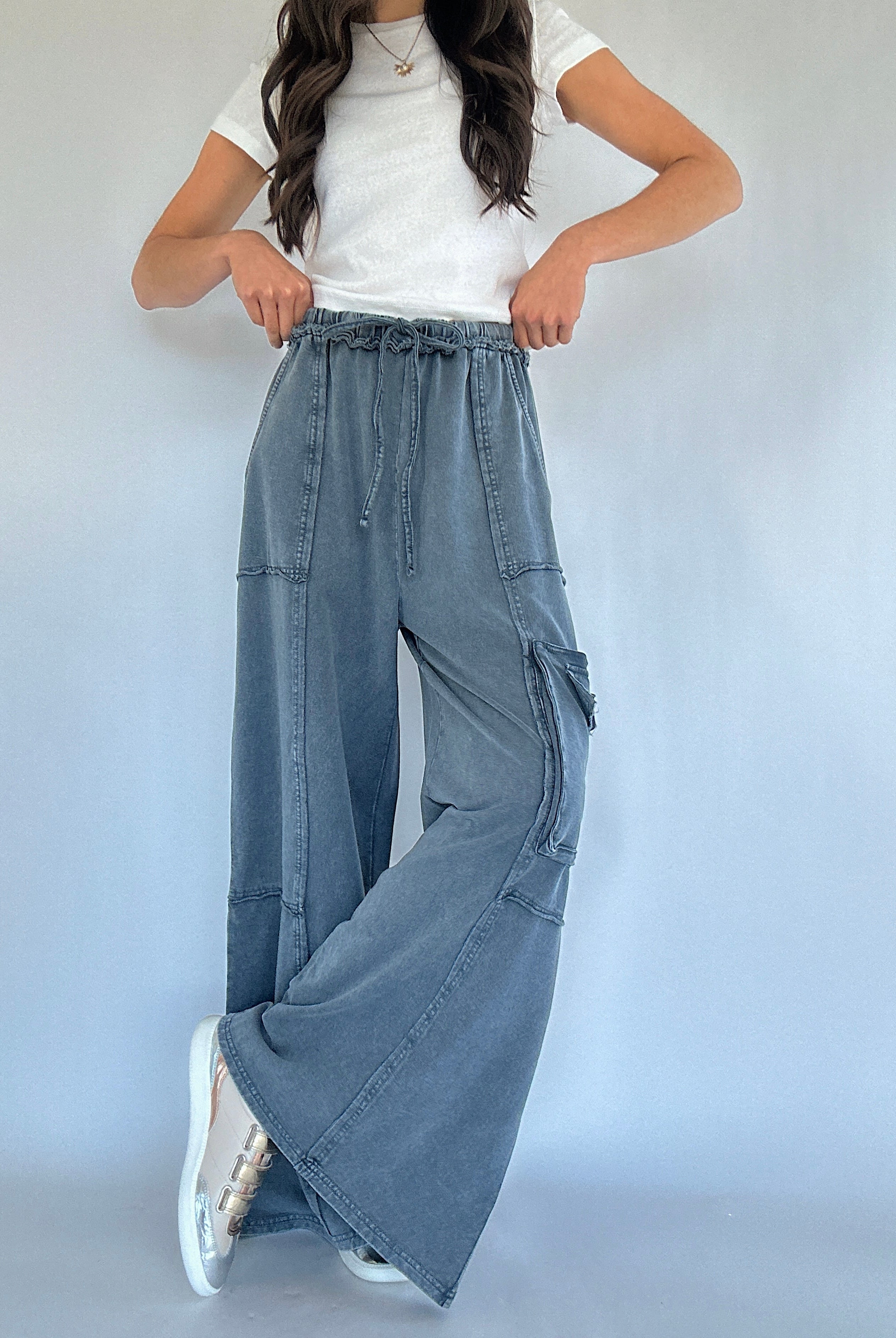 Person wearing smoke blue cargo pants and a white top on a plain background