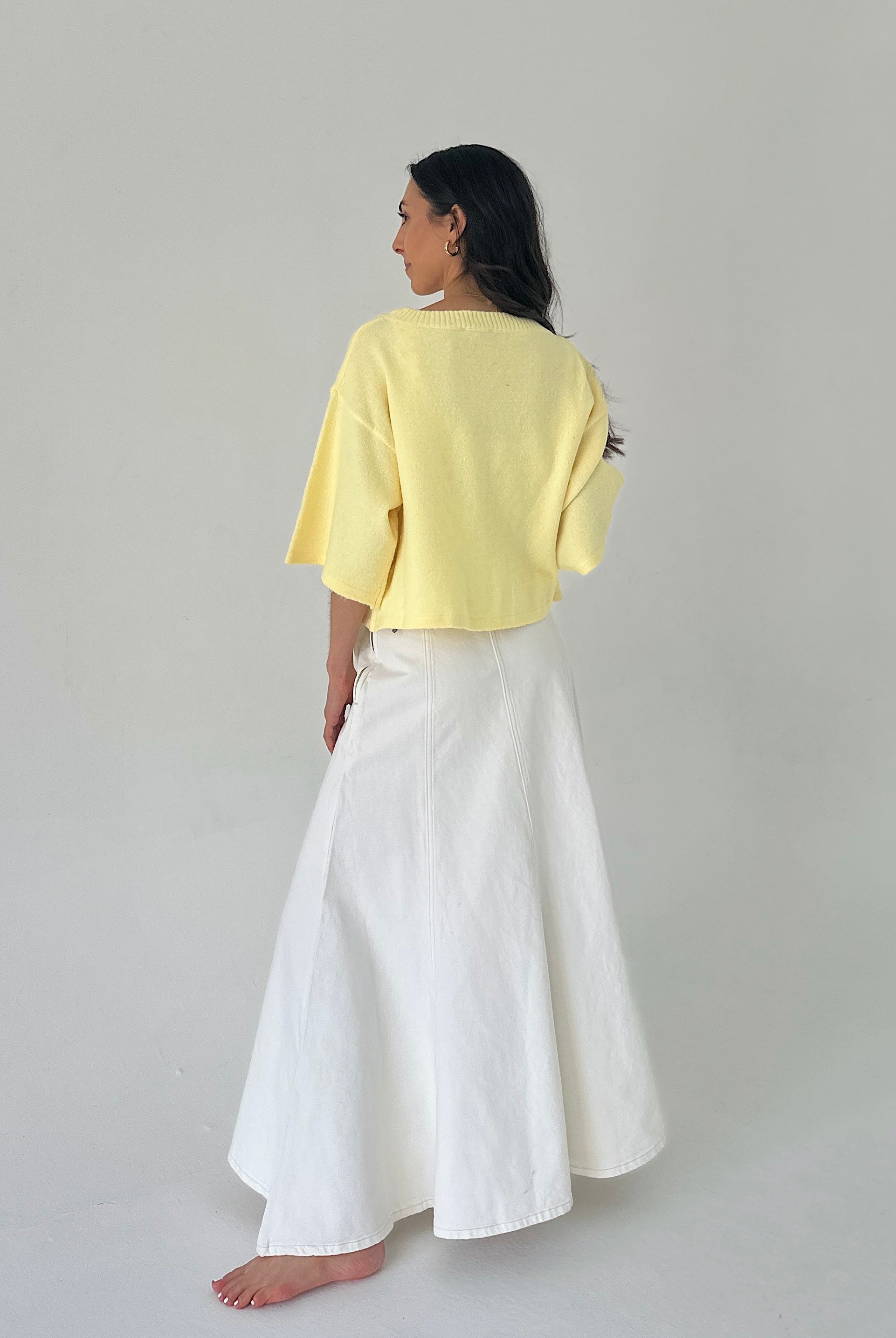 Woman wearing a yellow top and white pants on a plain background