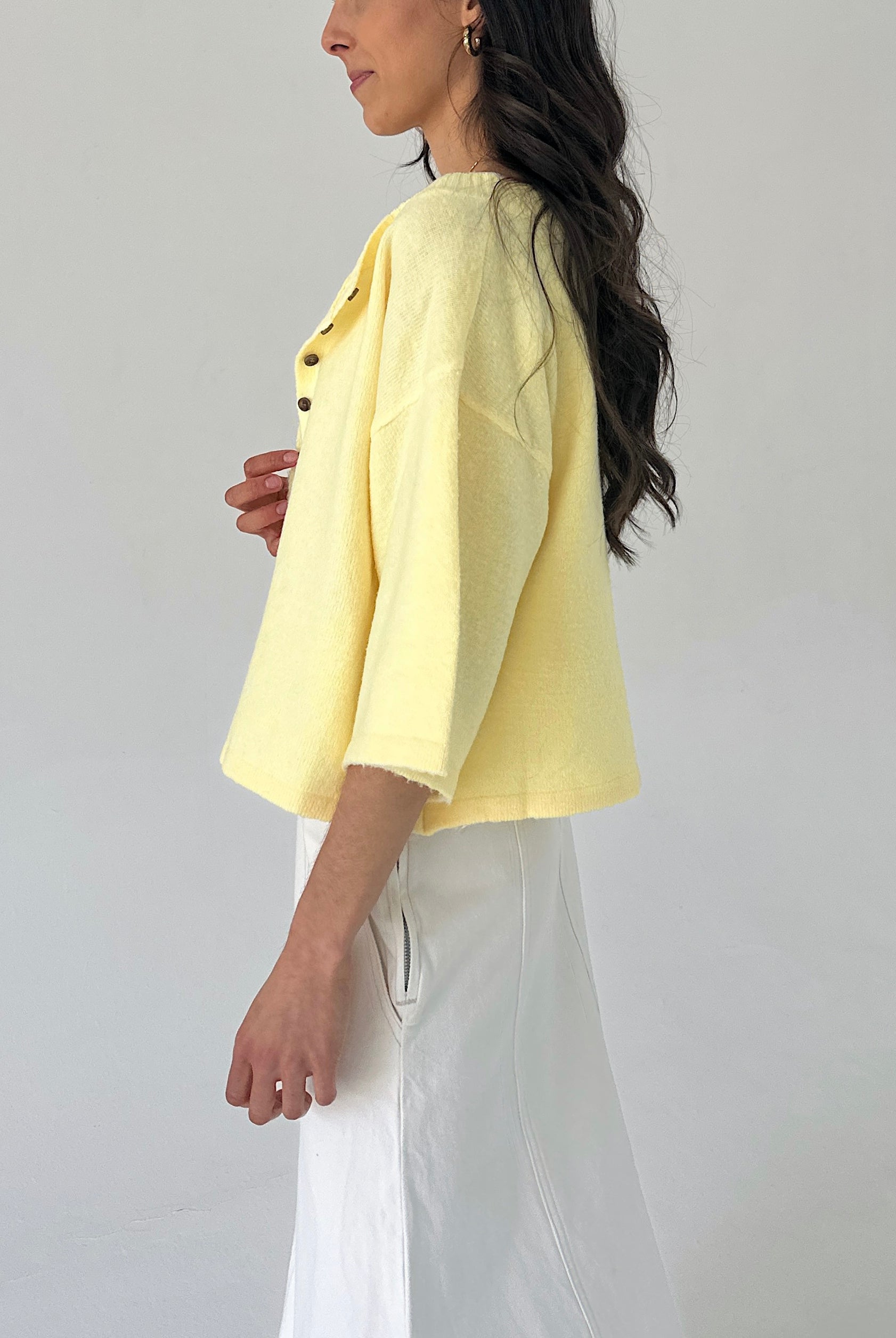 Woman wearing a light yellow cardigan and white pants against a plain background from side