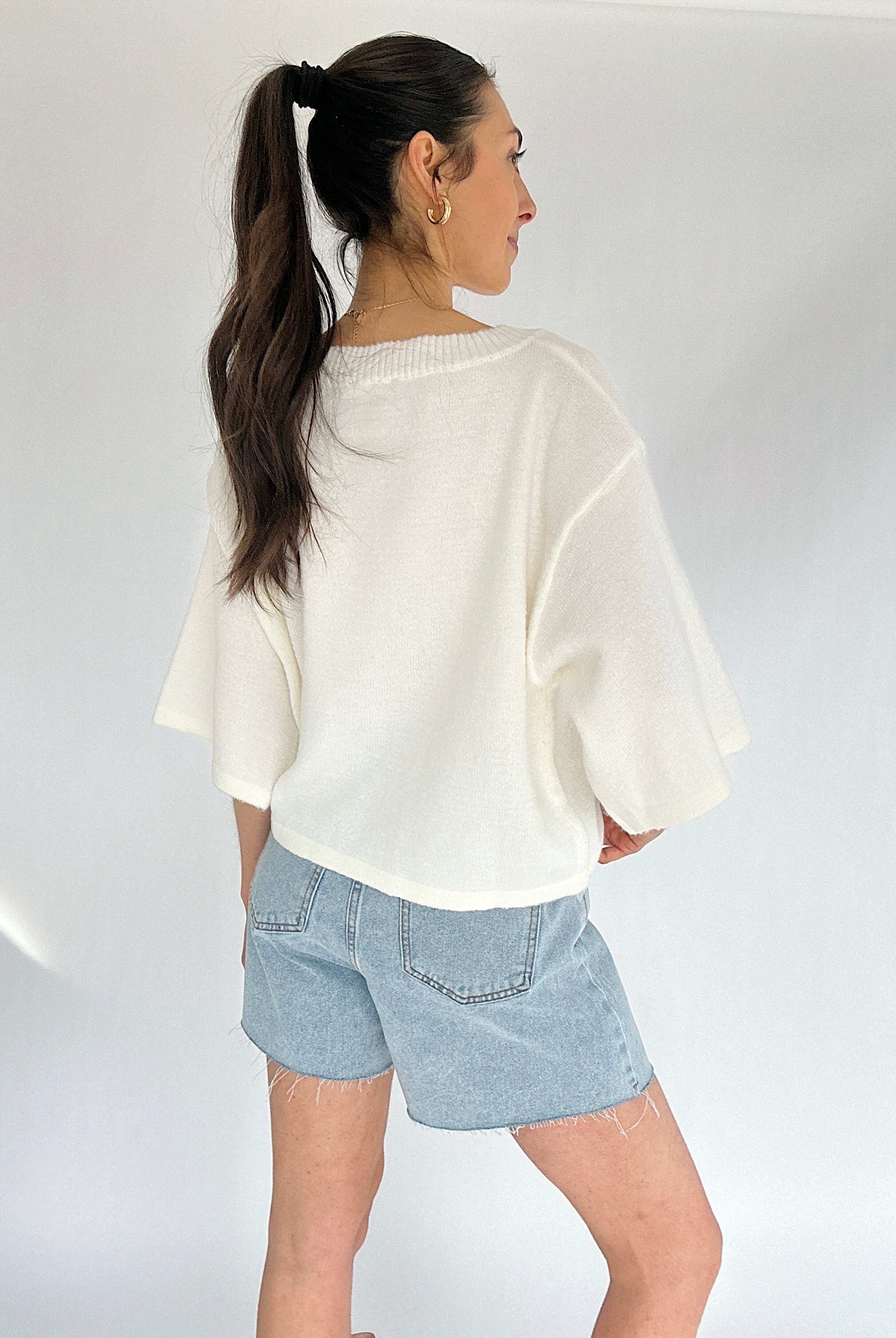 Woman wearing a white sweater and light blue denim shorts on a plain background