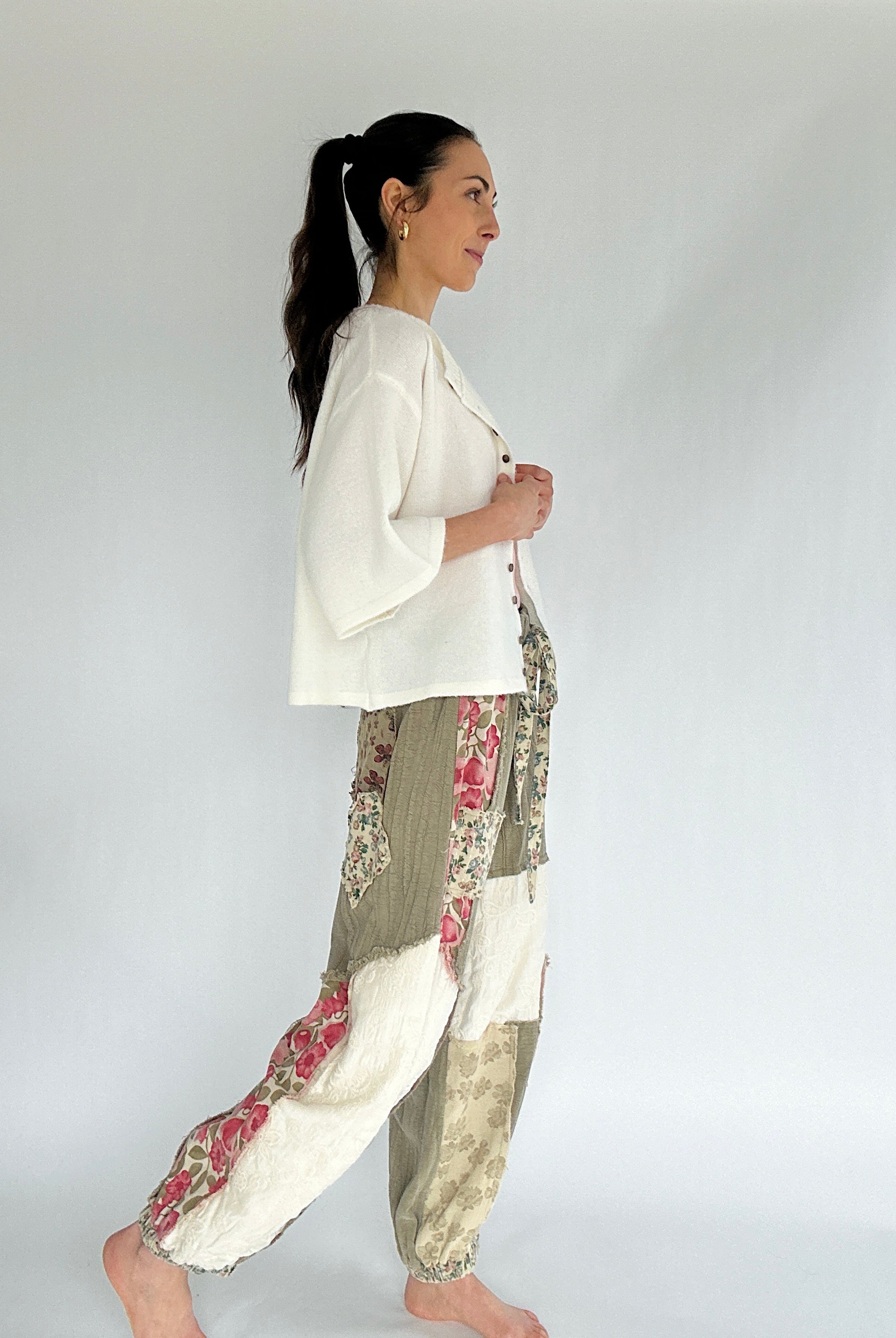 Woman wearing a white top and floral pants against a plain background from side