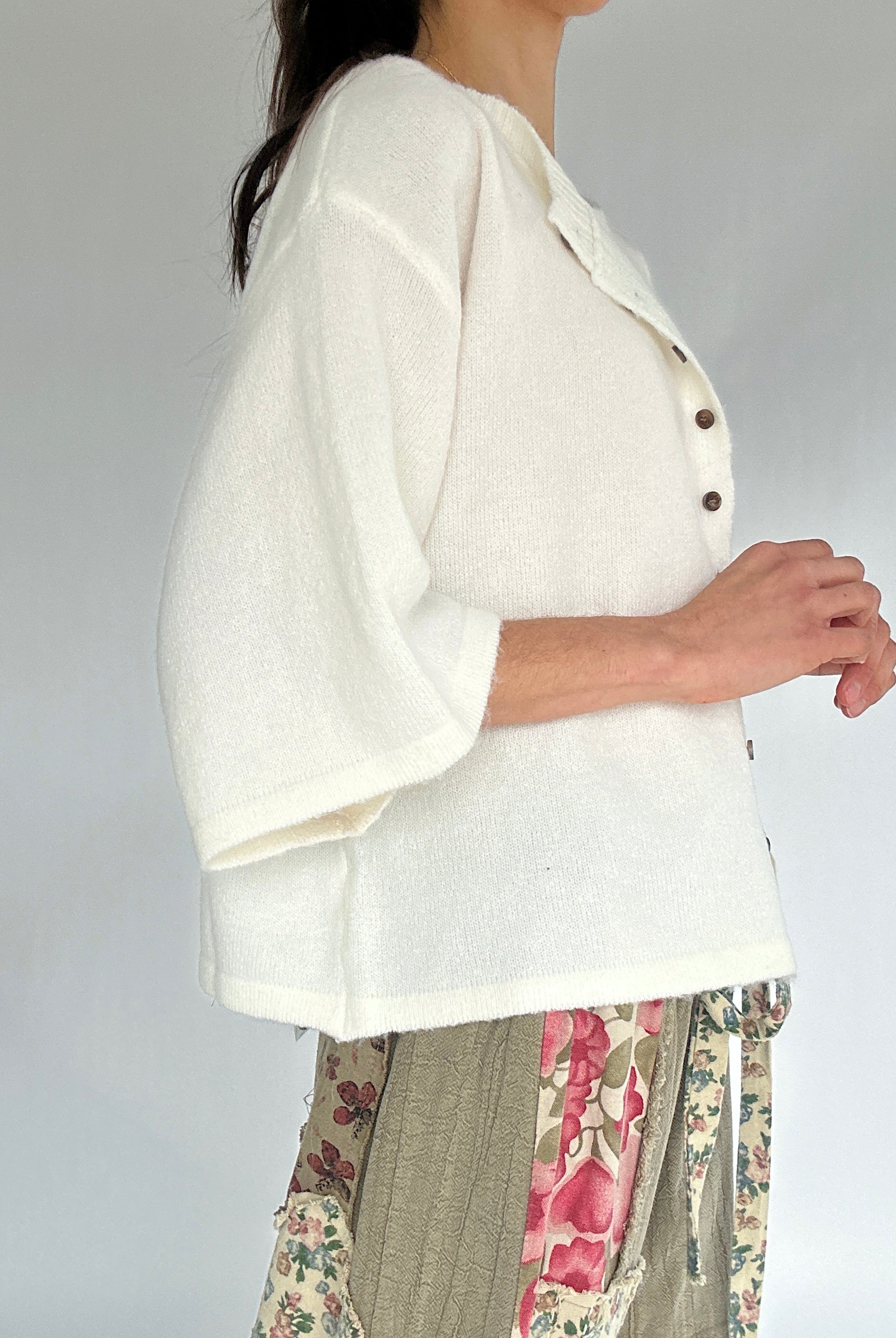 Person wearing a white cardigan with floral pants on a plain background from side