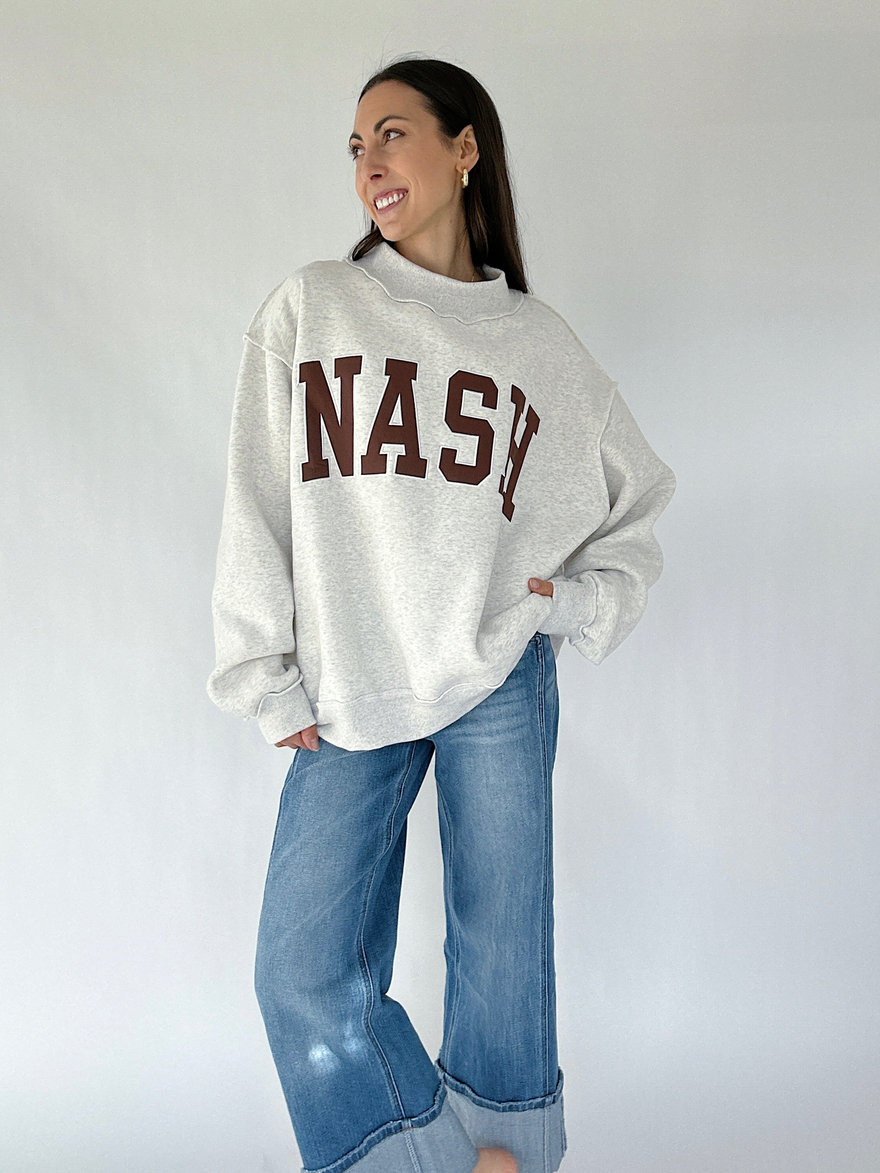 Person wearing a gray sweatshirt with 'NASH' printed on it, standing against a white background.
