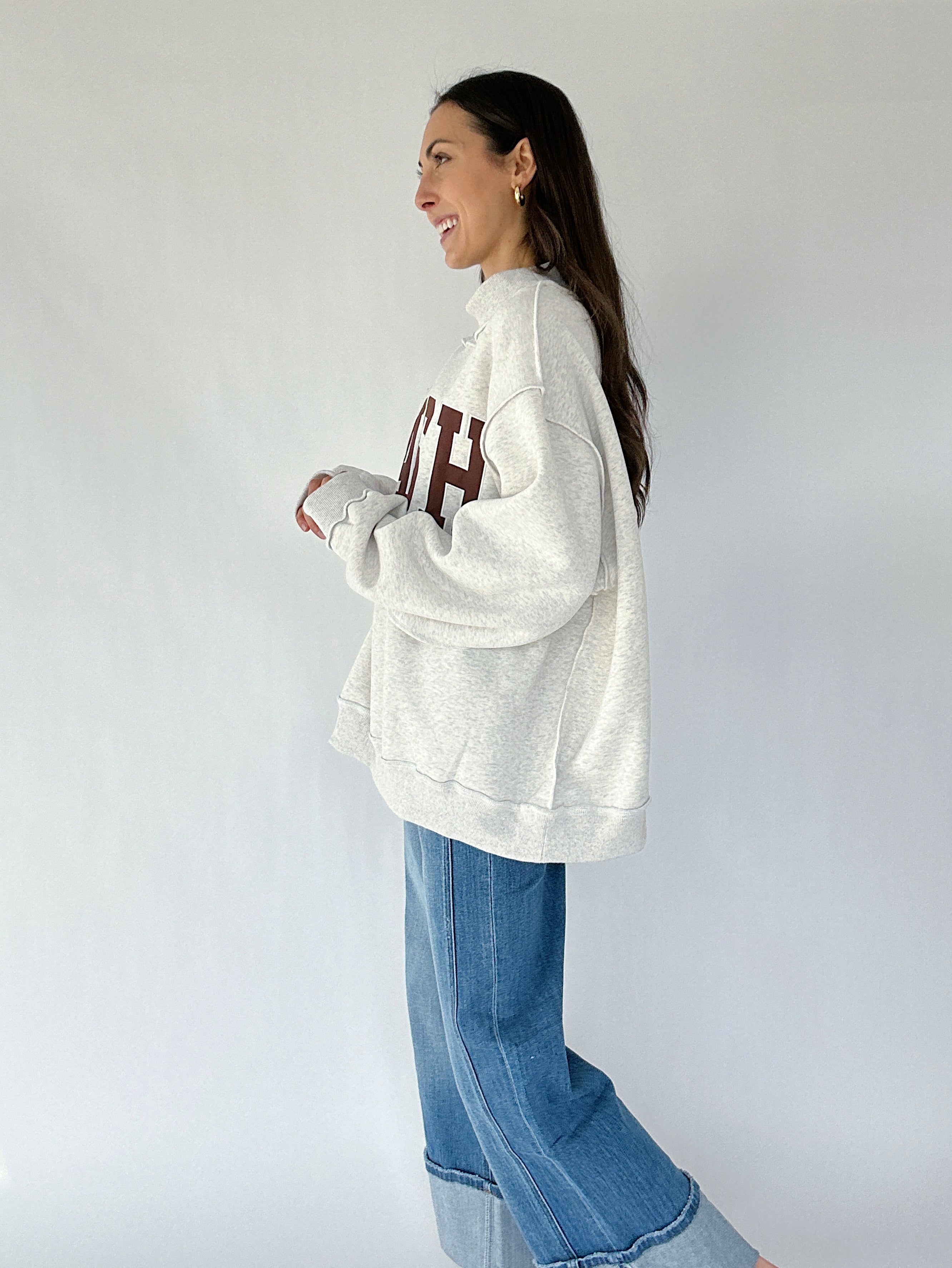 Woman wearing a grey oversized sweatshirt and blue jeans against a plain background