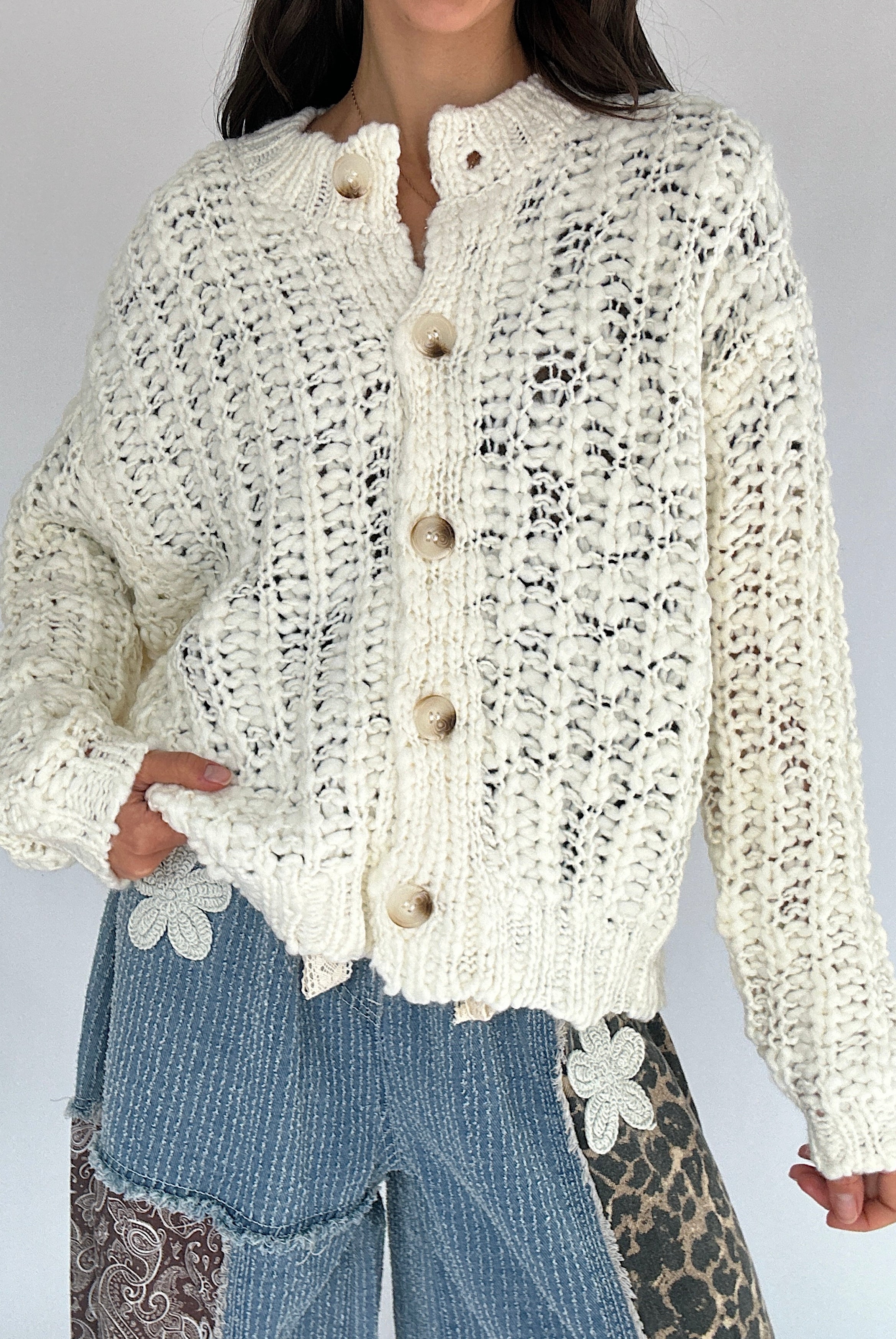 Person wearing a cream knitted button up cardigan with a plain background