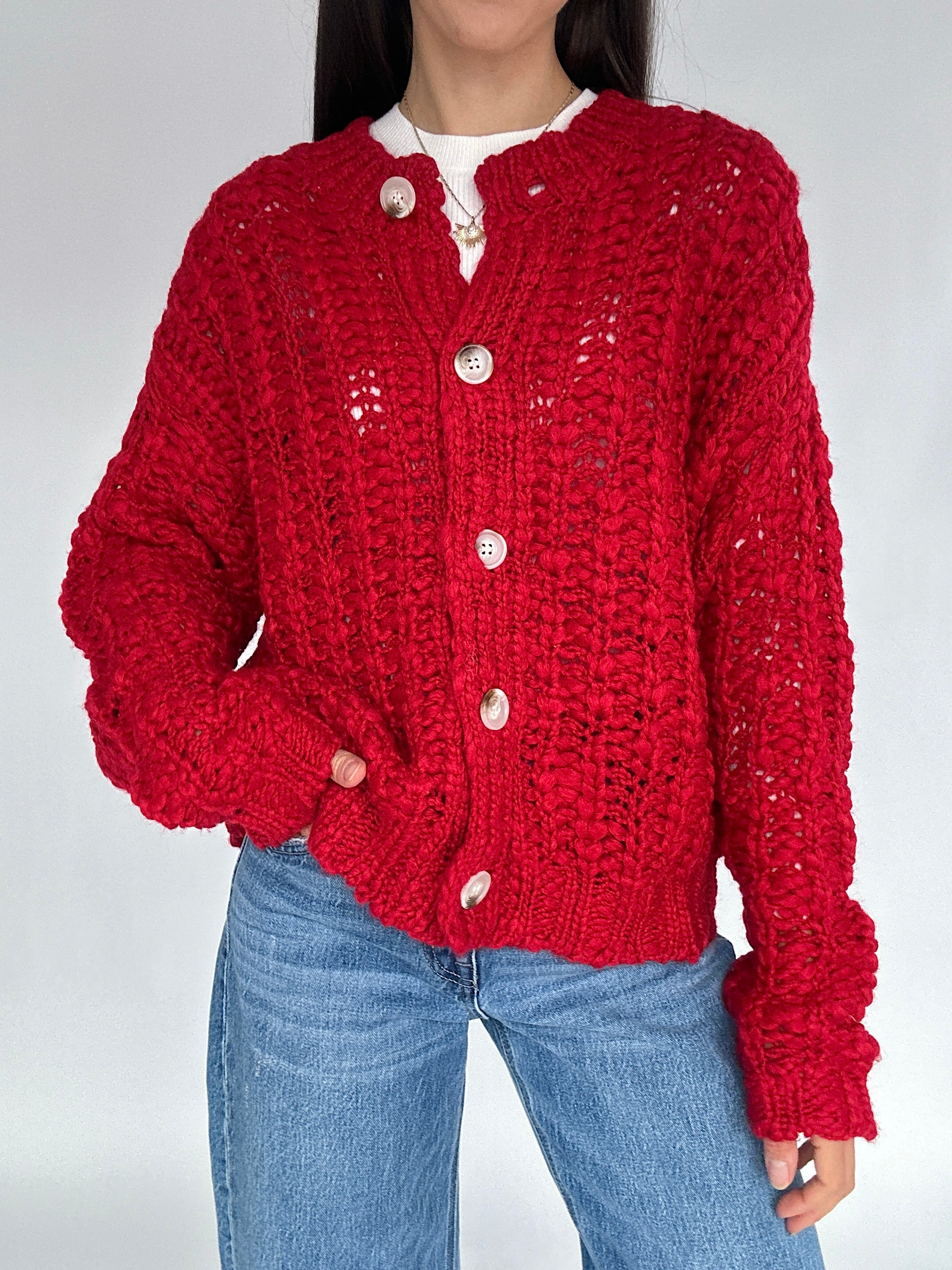 Person wearing a red knitted cardigan and blue jeans on a white background