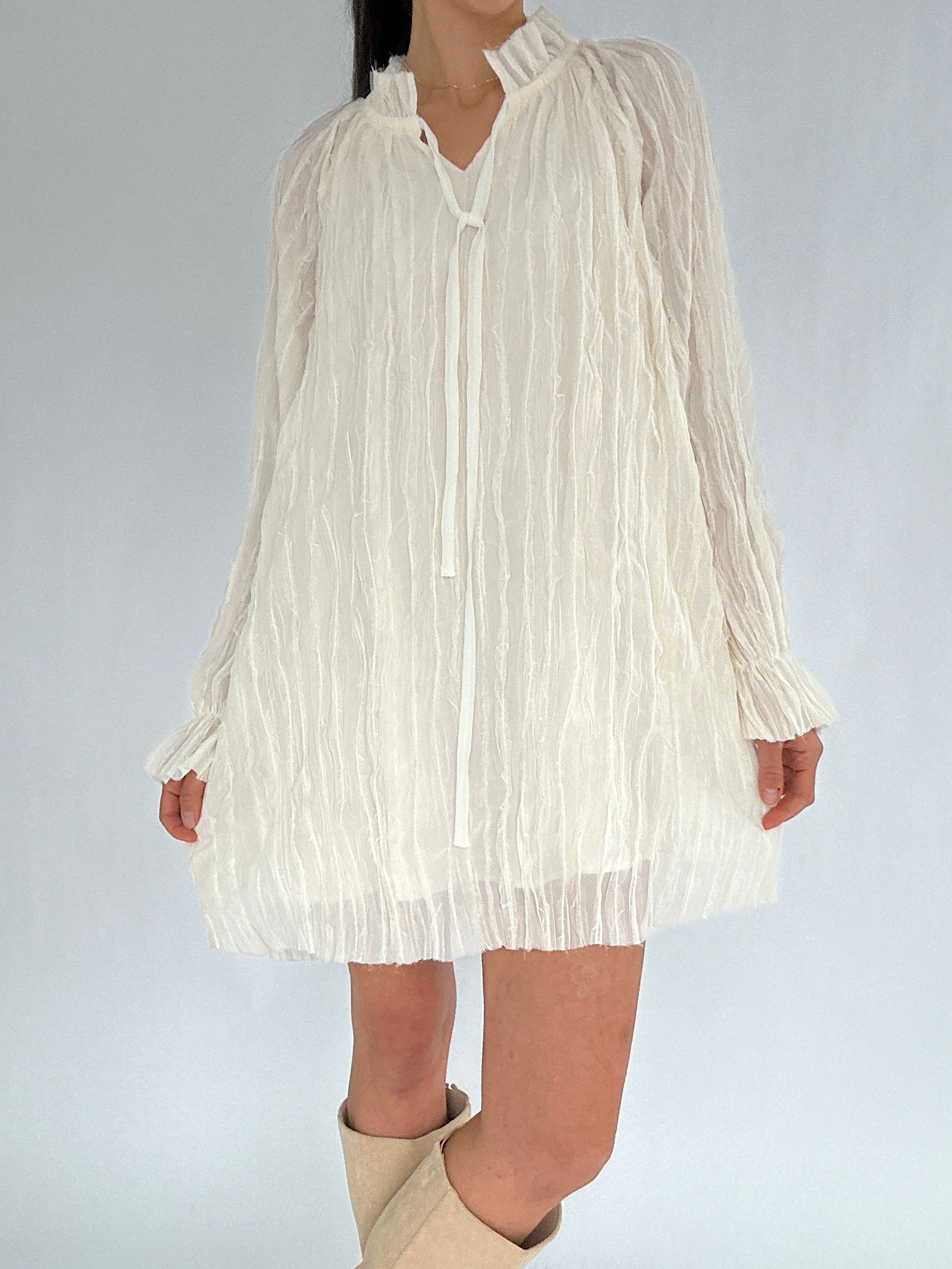 White pleated dress worn by a person on a plain background