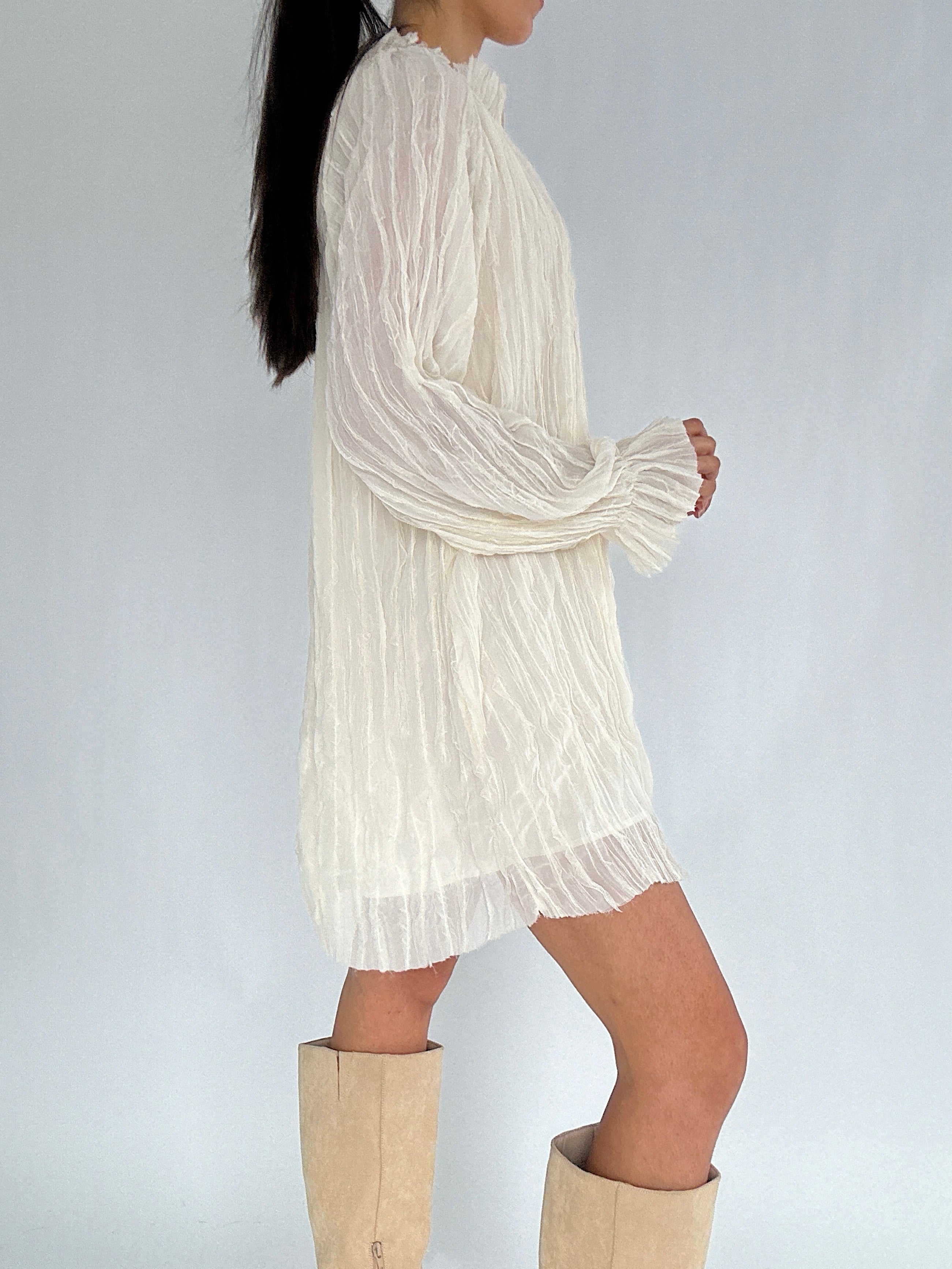 Person wearing a white long-sleeve dress with beige knee-high boots on a plain background