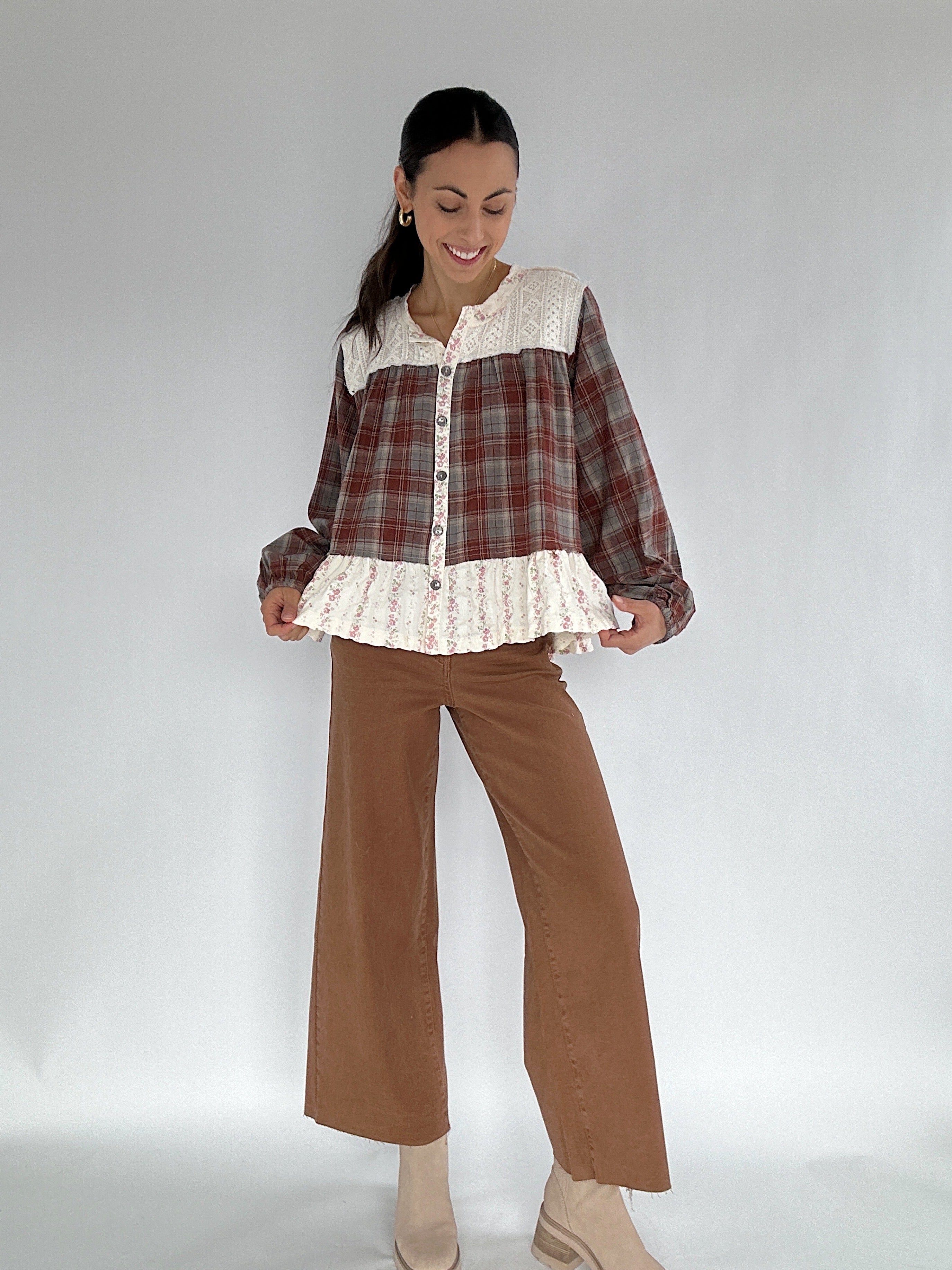 Woman wearing a plaid shirt with lace trim and brown pants on a white background