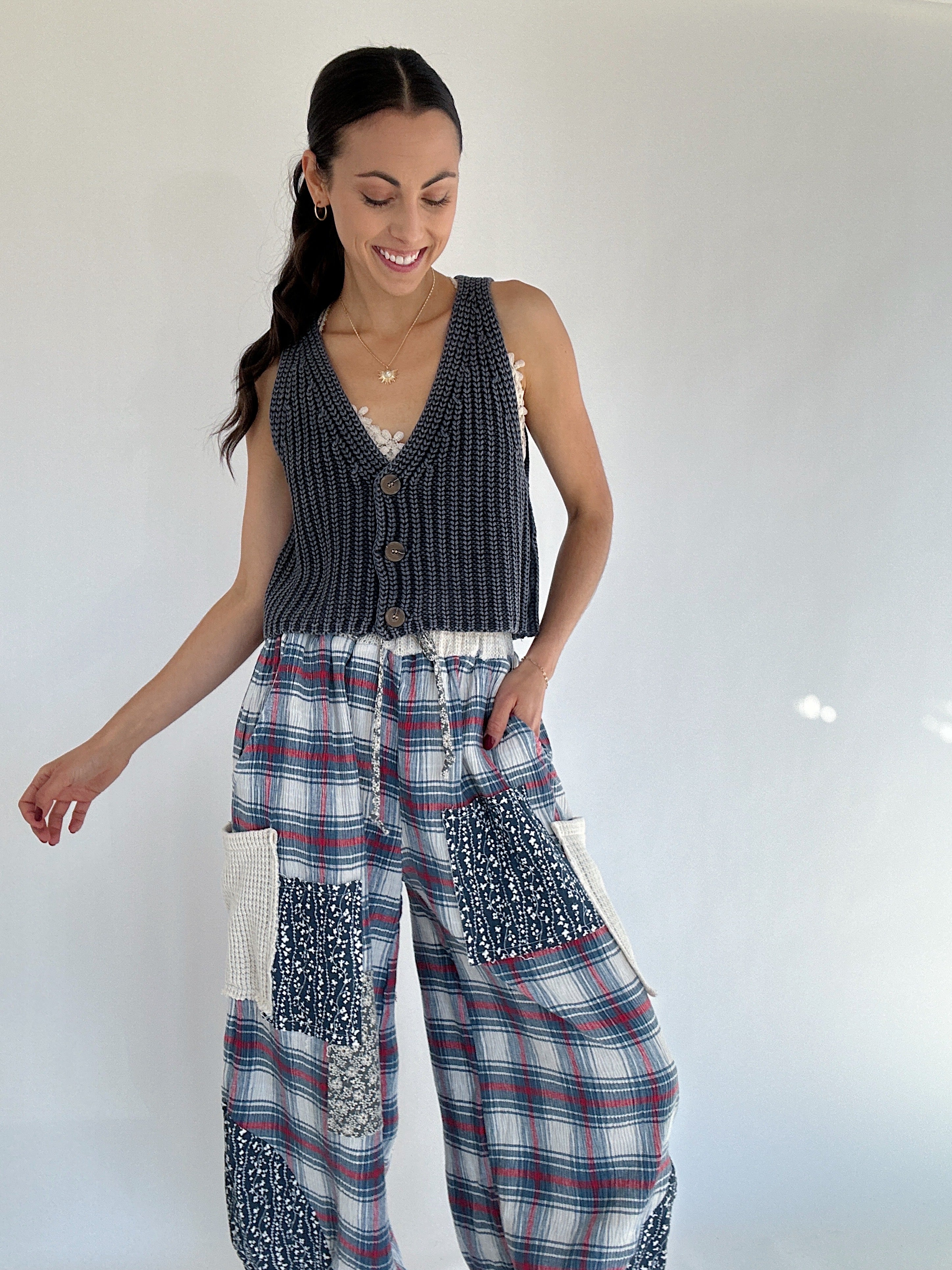 Woman wearing a navy sleeveless knit vest top and plaid pants with a white background