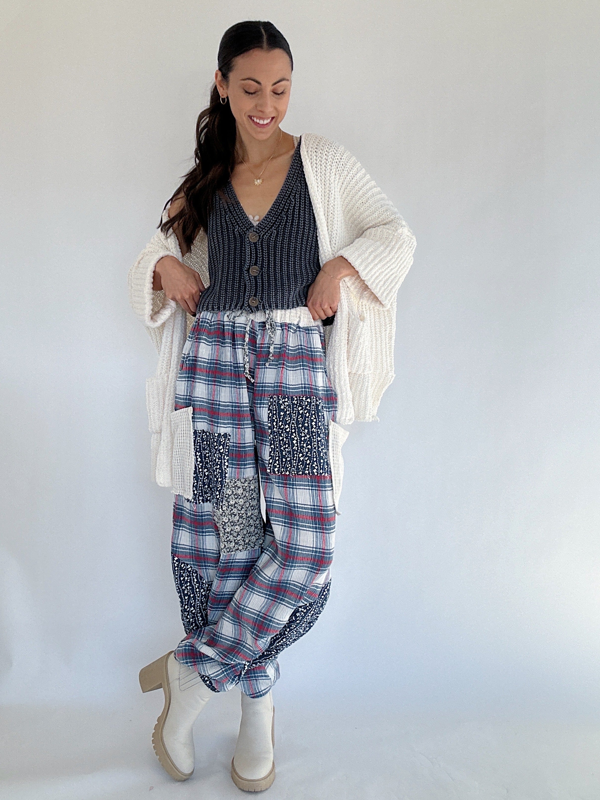 Woman wearing a white cardigan, navy knit vest top, and plaid pants against a white background