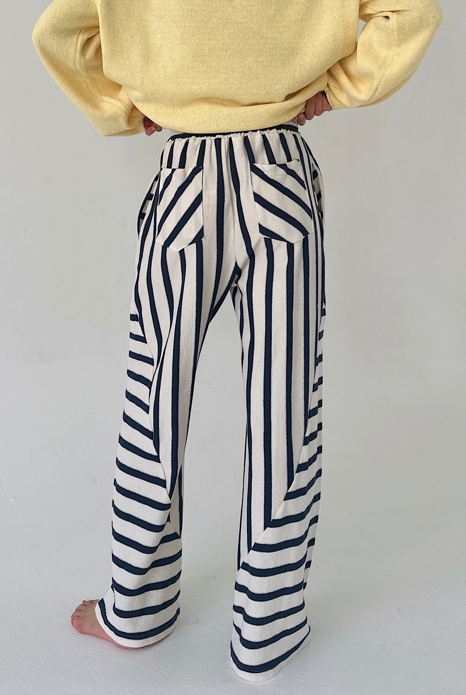 Person wearing a yellow sweater and black and white striped pants on a plain background showing back