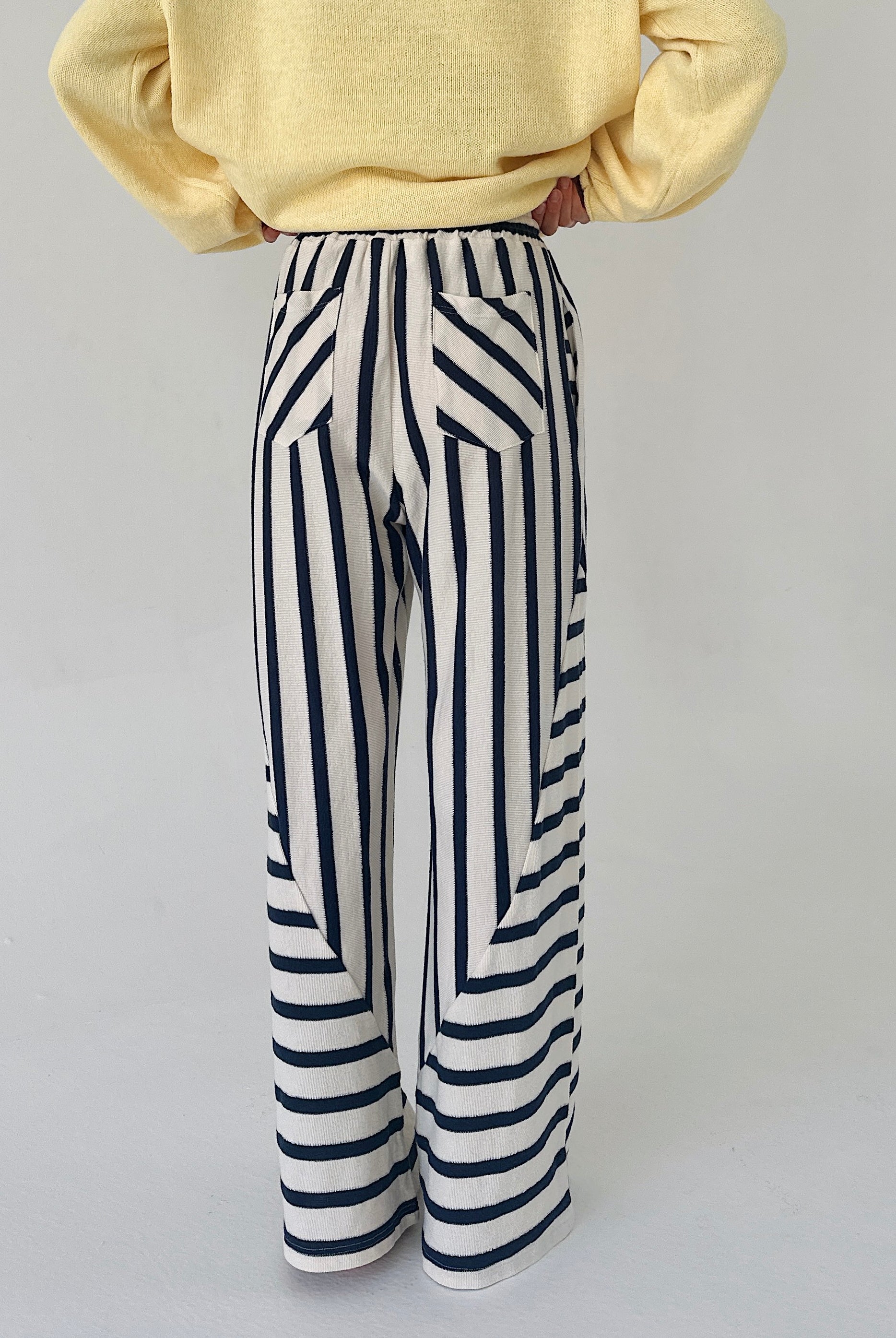 Person wearing a yellow sweater and black and white striped pants on a light gray background showing back