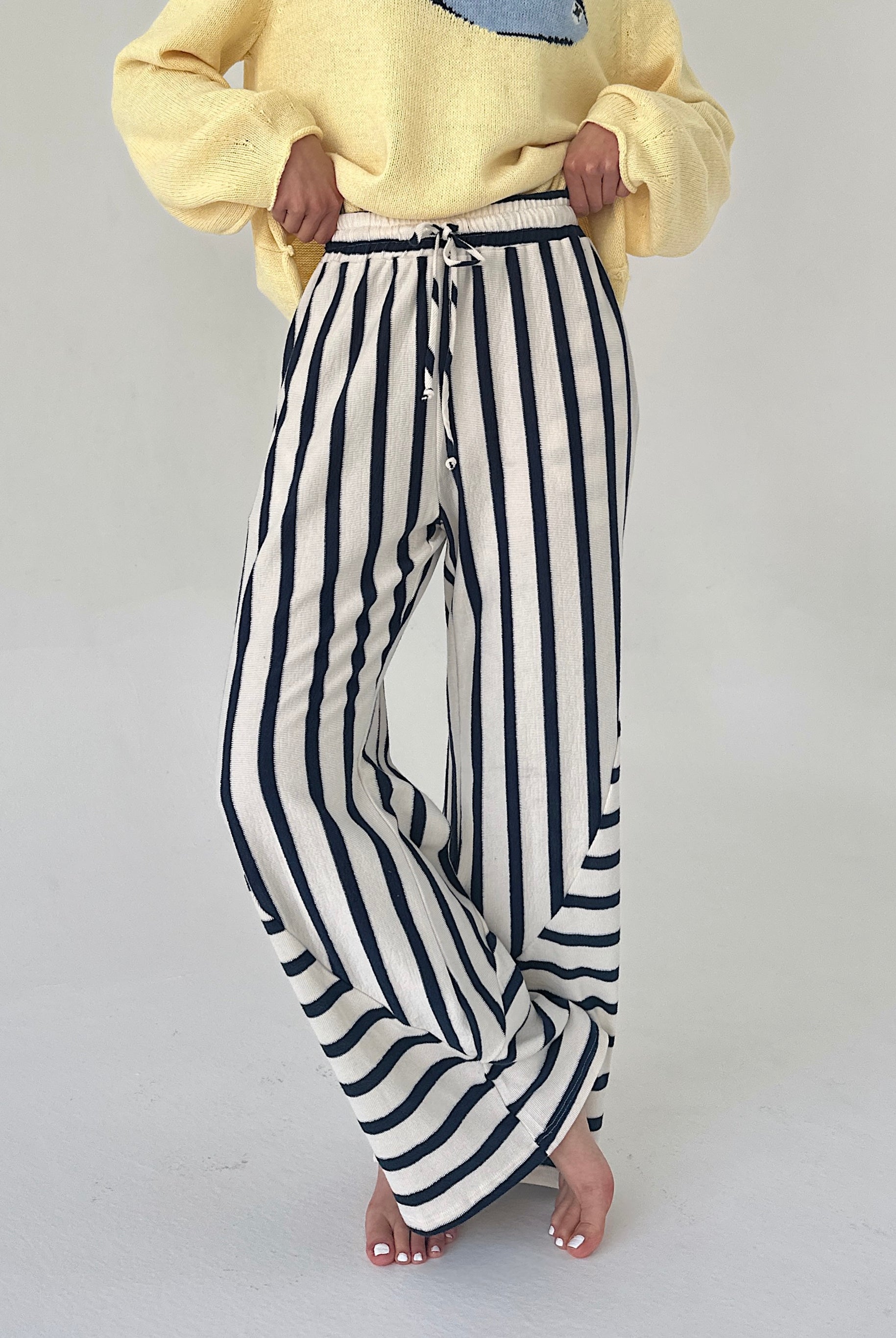 Person wearing a yellow sweater and black and white striped pants on a plain background