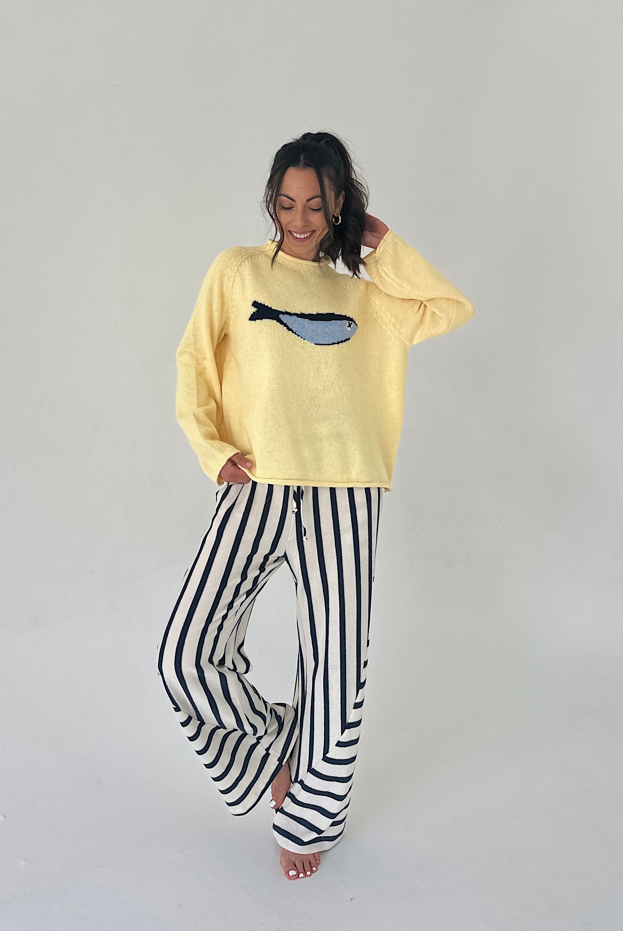 Person wearing a yellow sweater with a fish design and black and white striped pants on a plain background