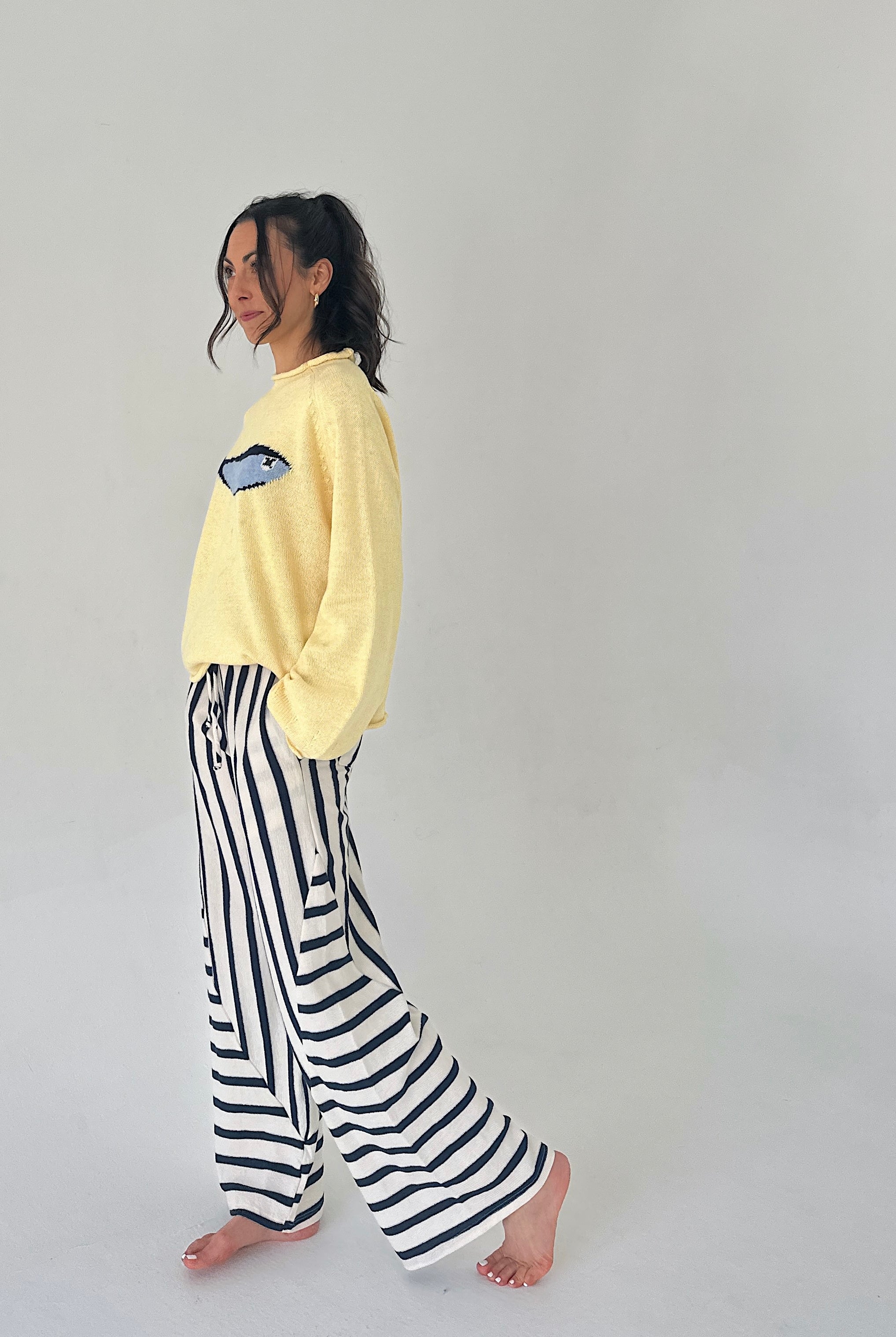 Person wearing a yellow sweater and black and white striped pants on a plain background