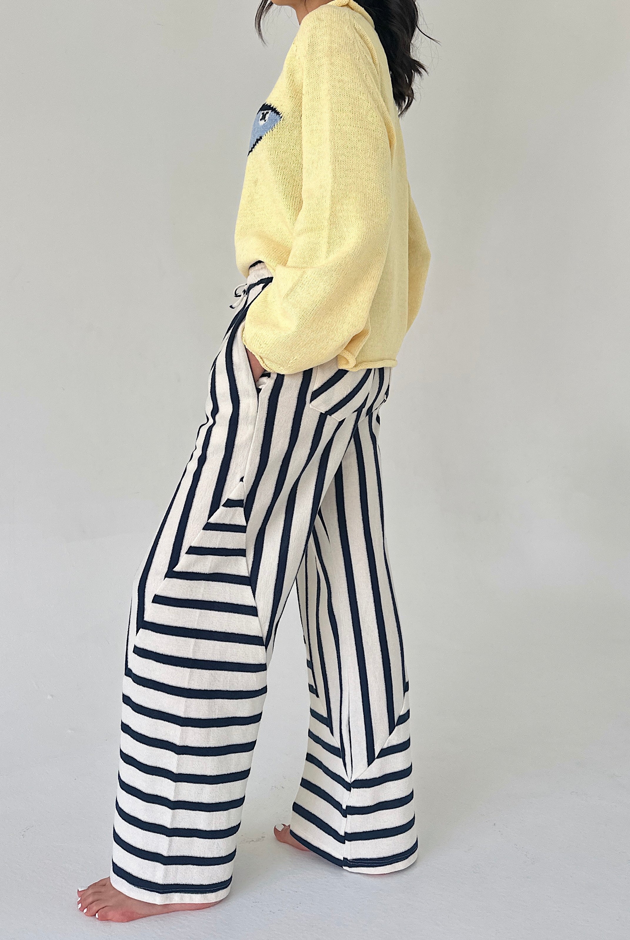 Person wearing a yellow sweater and black and white striped pants on a plain background from side
