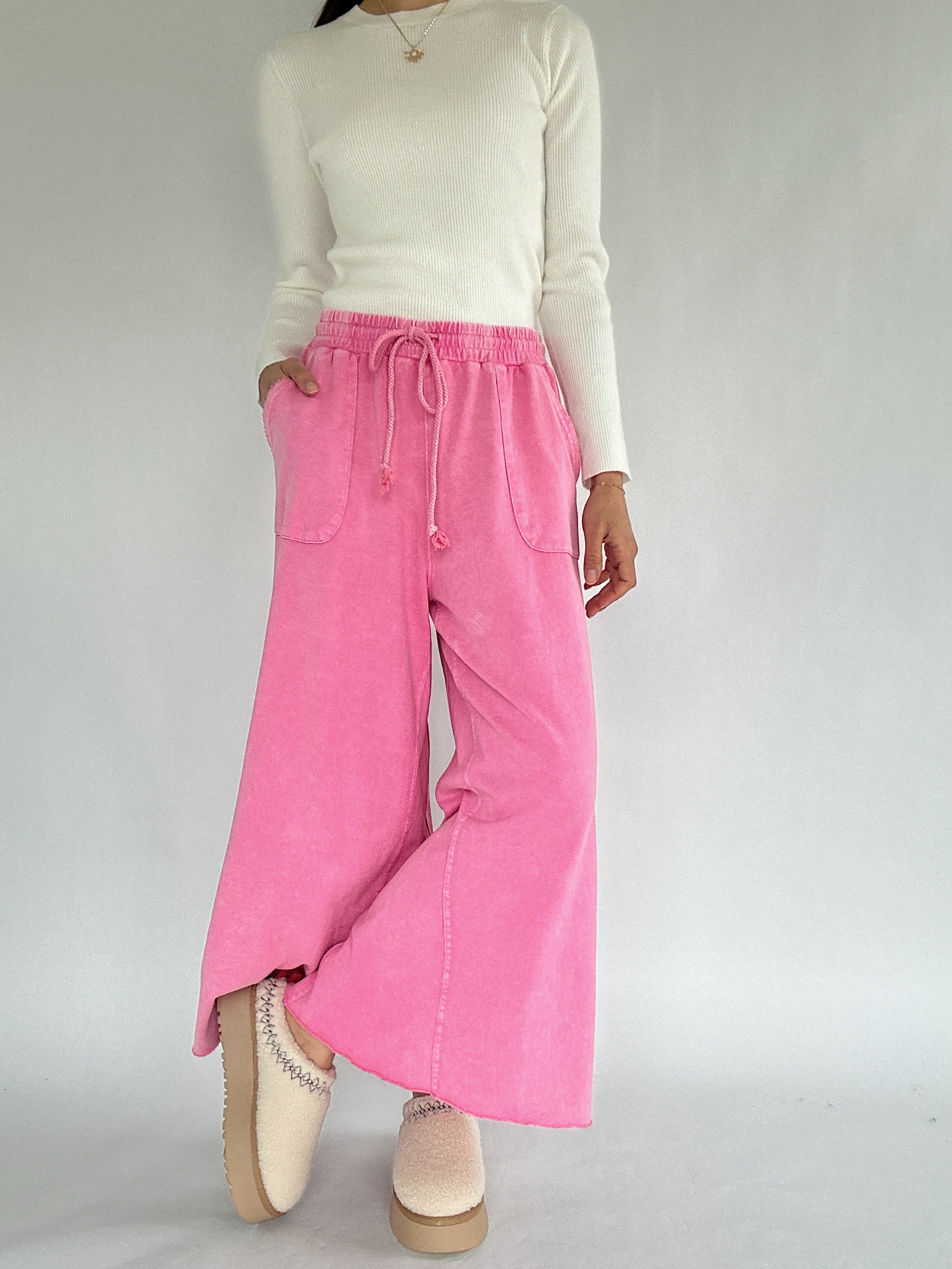 Person wearing a white long-sleeve top and pink wide-leg pants on a plain background