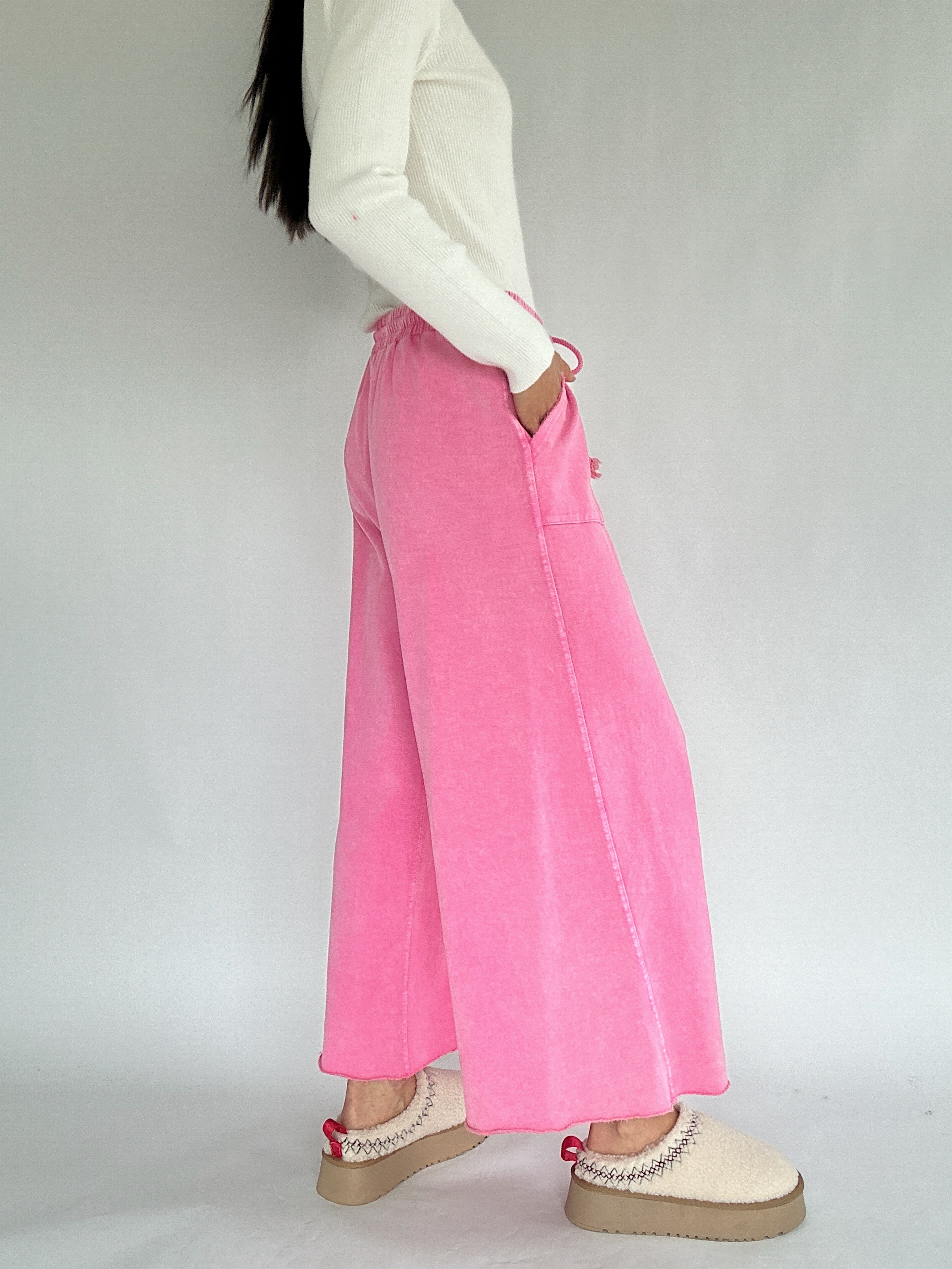 Person wearing bright pink wide leg sweatpants and white clogs on a plain background from side