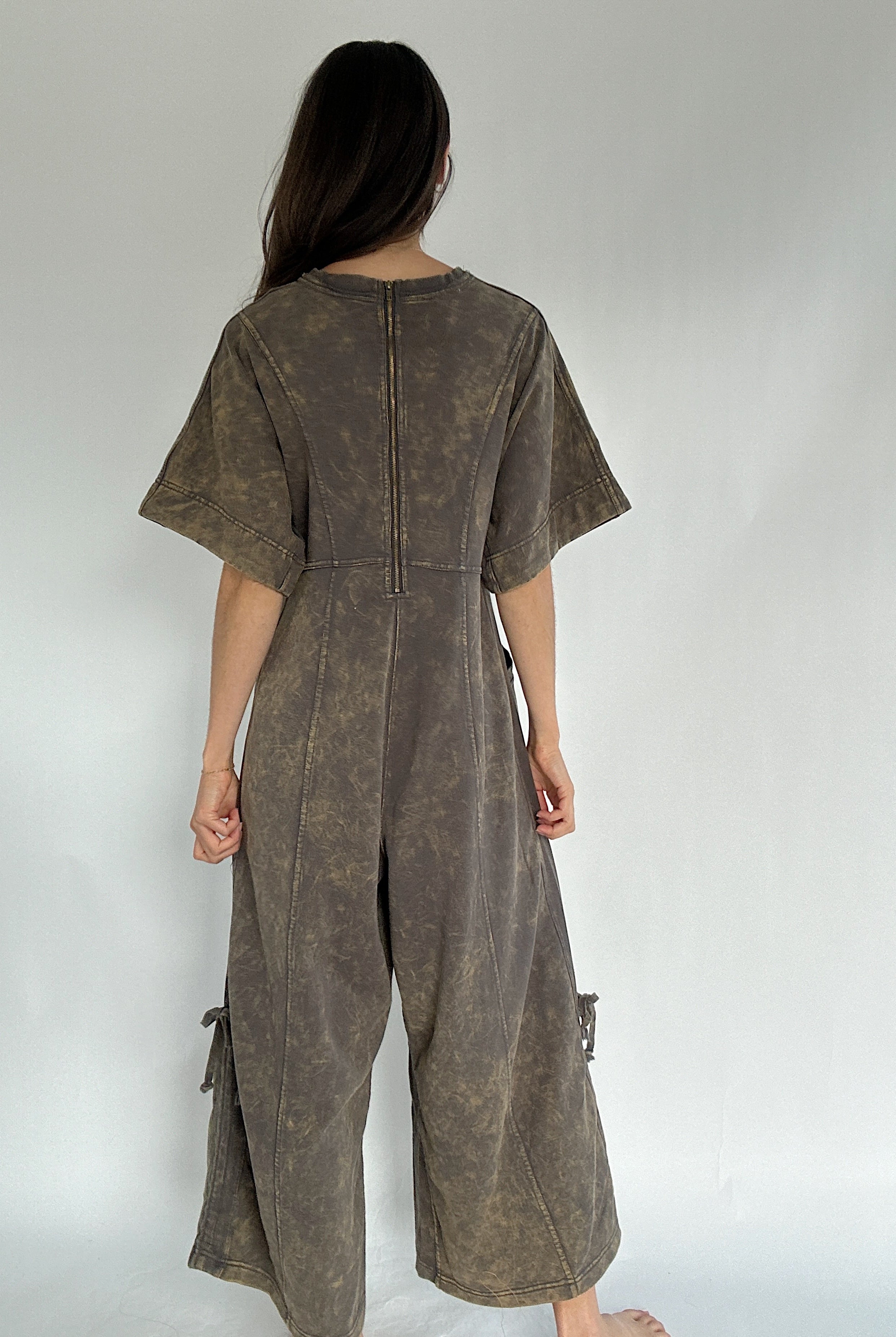 Person wearing a brown jumpsuit against a plain background to show back zip up feature