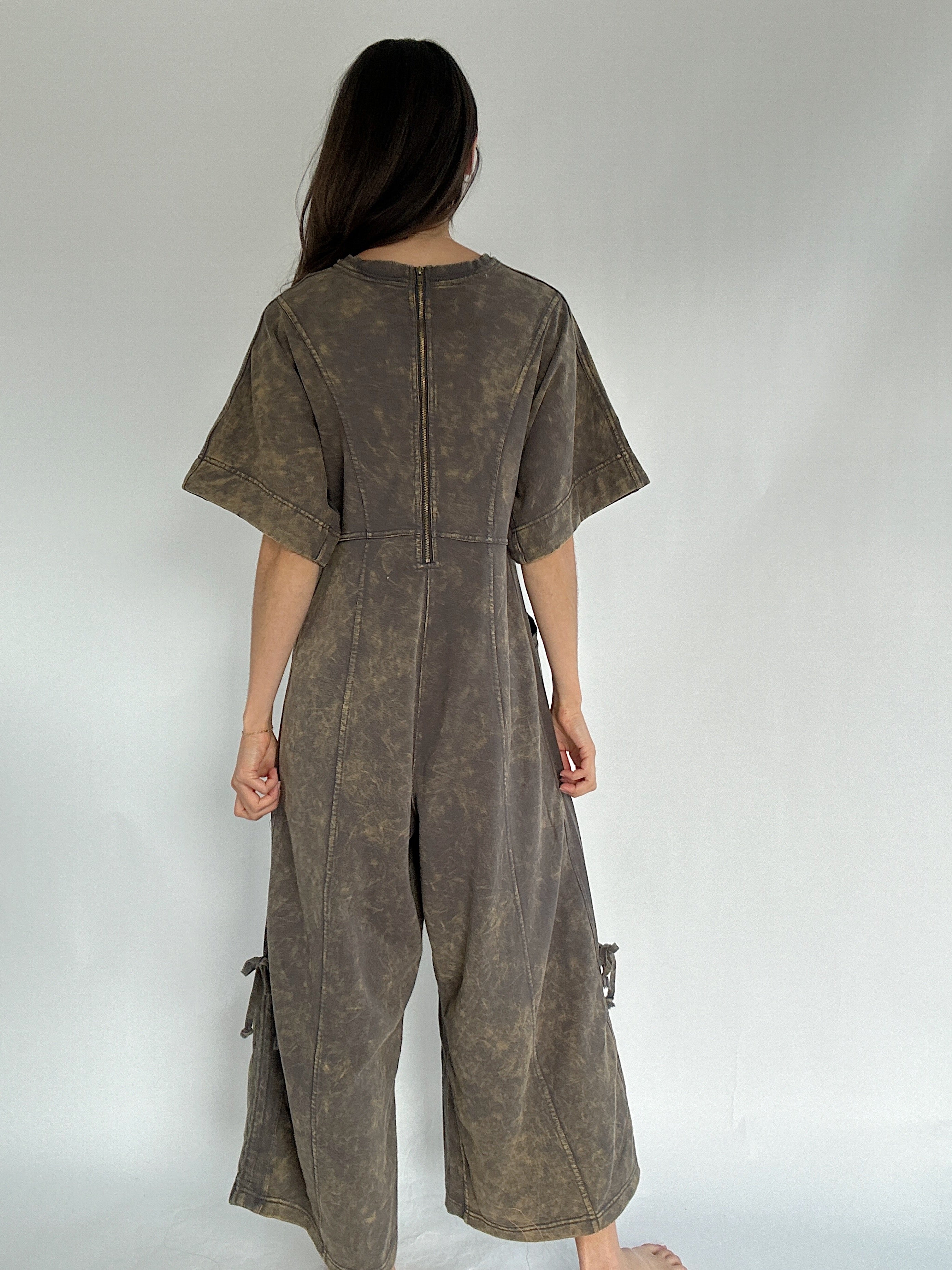 Person wearing a brown jumpsuit against a plain background to show back zip up feature