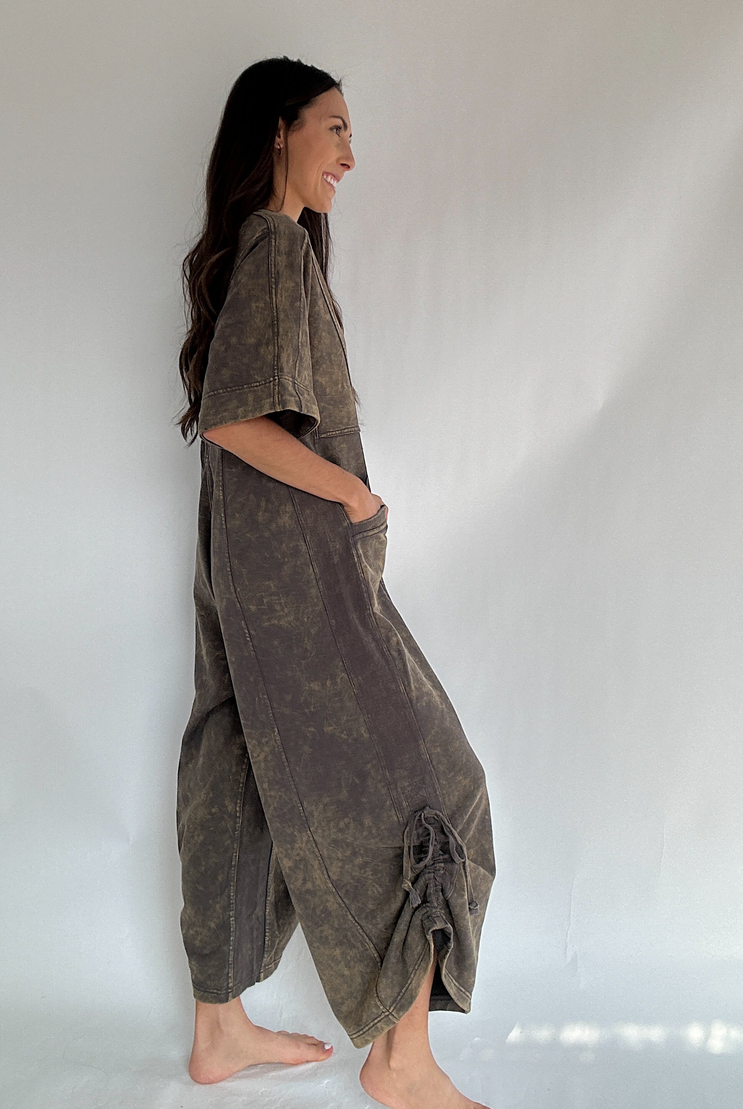 Woman wearing a brown jumpsuit against a white background to show side view